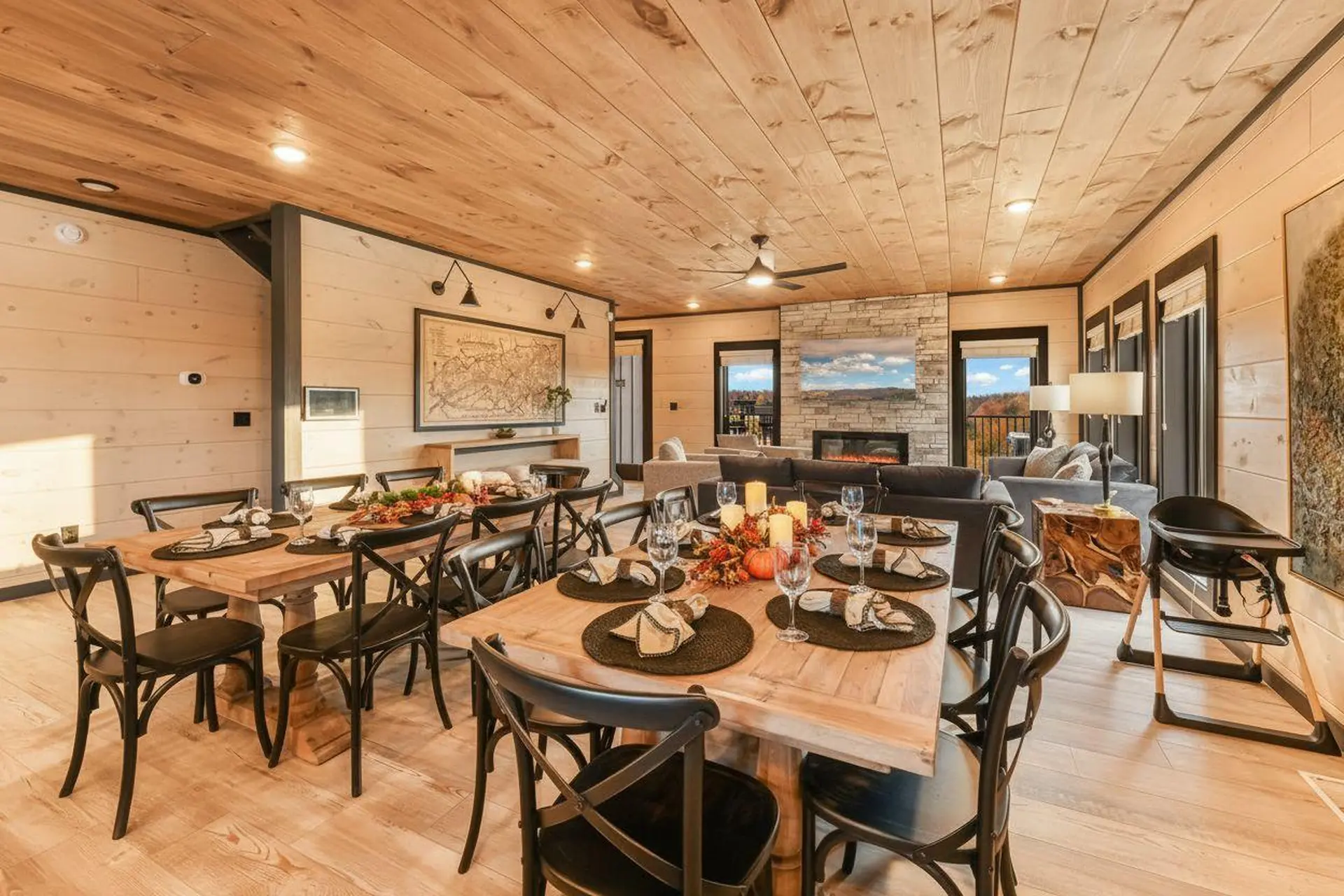 A rustic dining room with wood paneled walls and ceiling, a stone fireplace, and a dining table set 