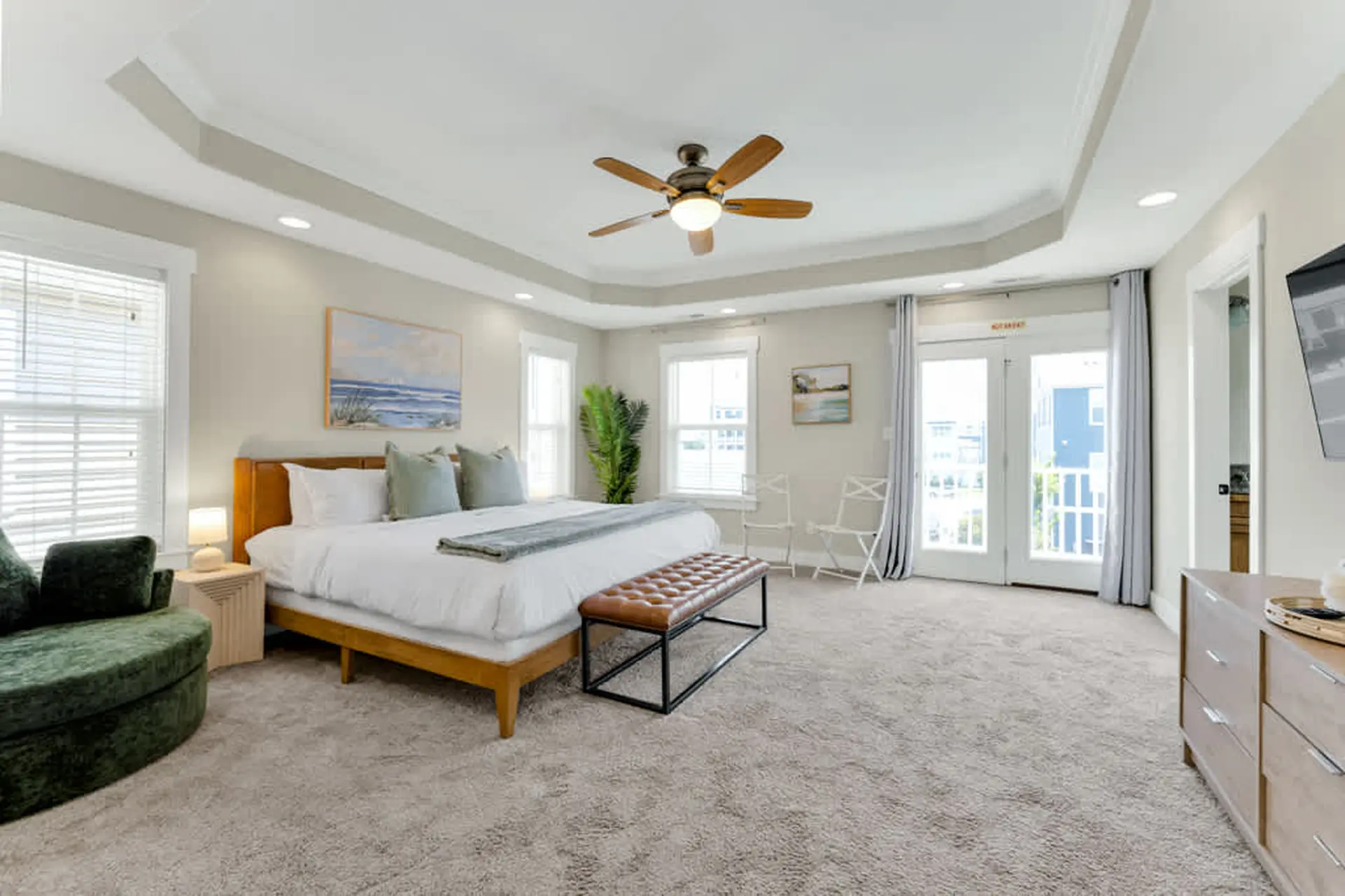 A spacious bedroom with a king bed, green chaise lounge, ceiling fan, and balcony access.