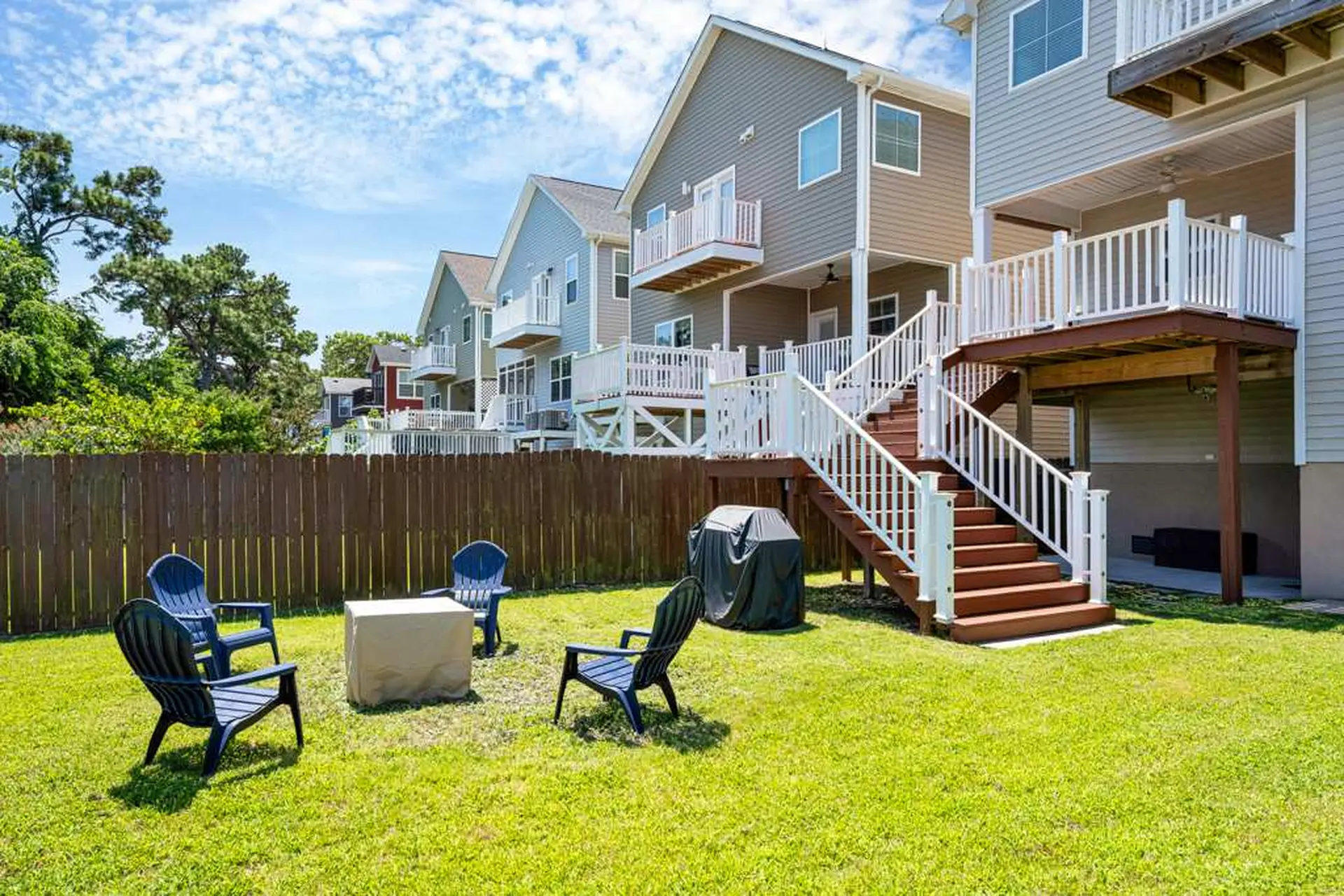 A vibrant backyard scene featuring a neatly mowed green lawn with blue Adirondack chairs arranged ar