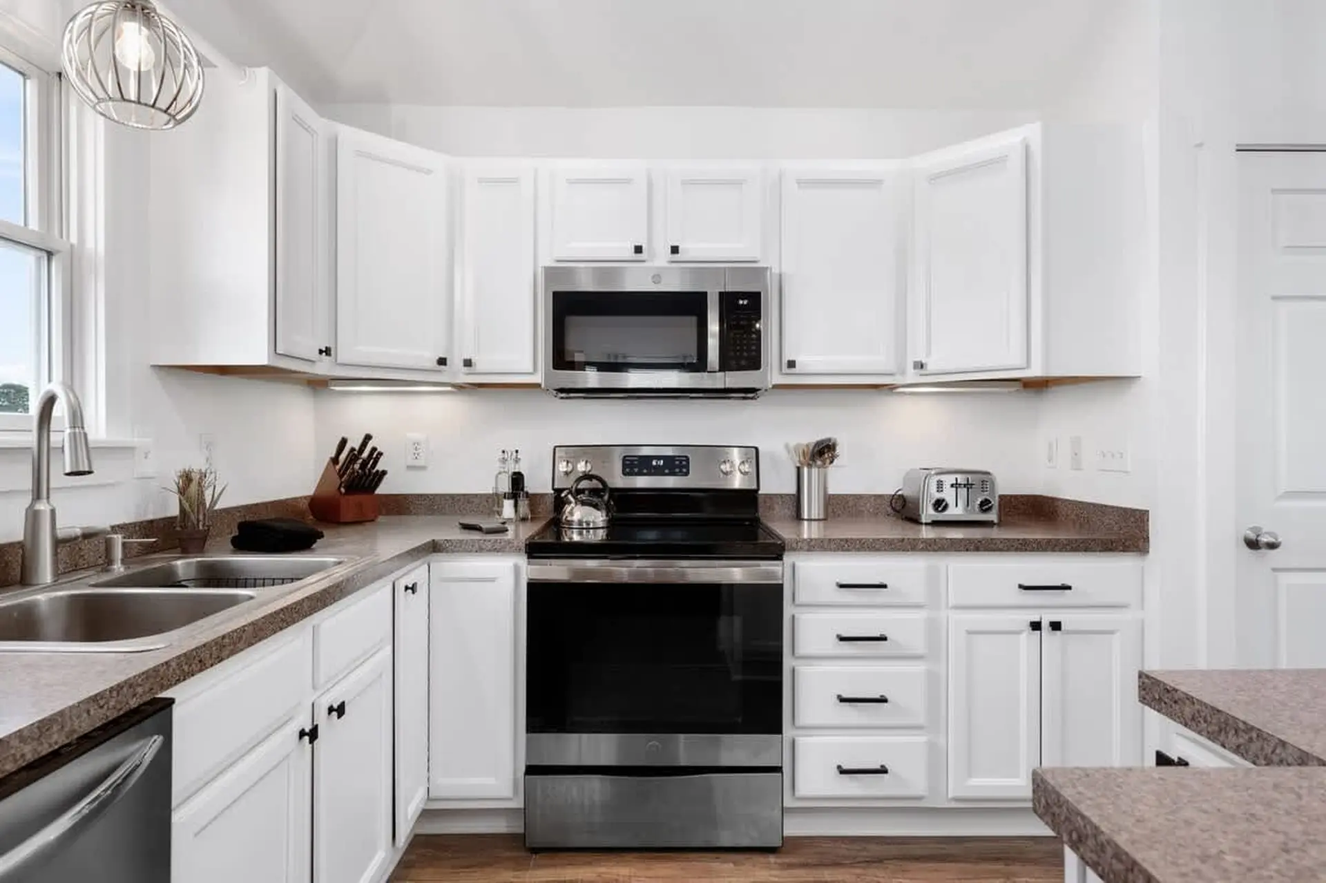 A stainless steel stove and microwave are the focal points of this clean, white kitchen.