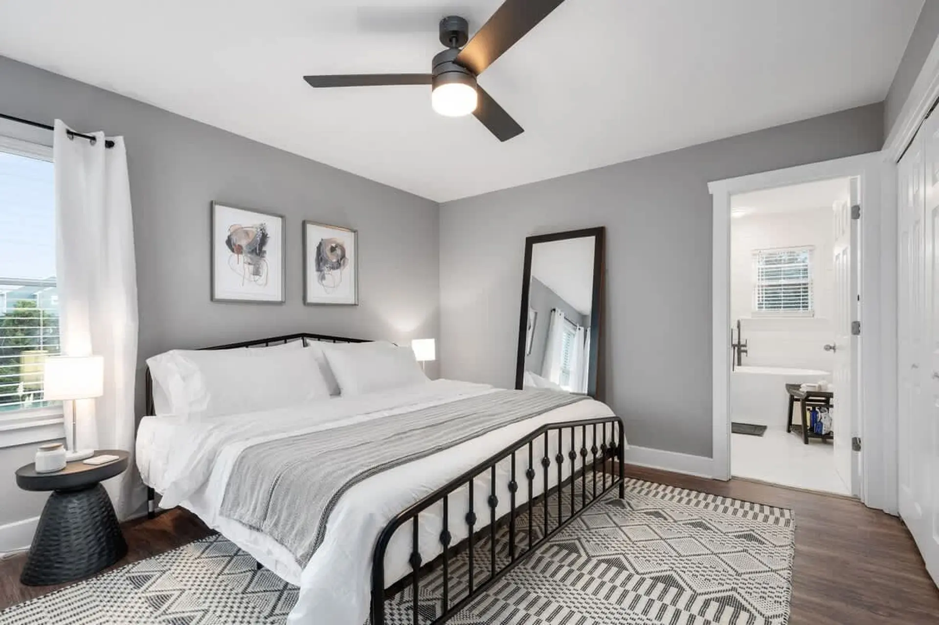 A bedroom with a black metal bed, grey blanket, and a large mirror.