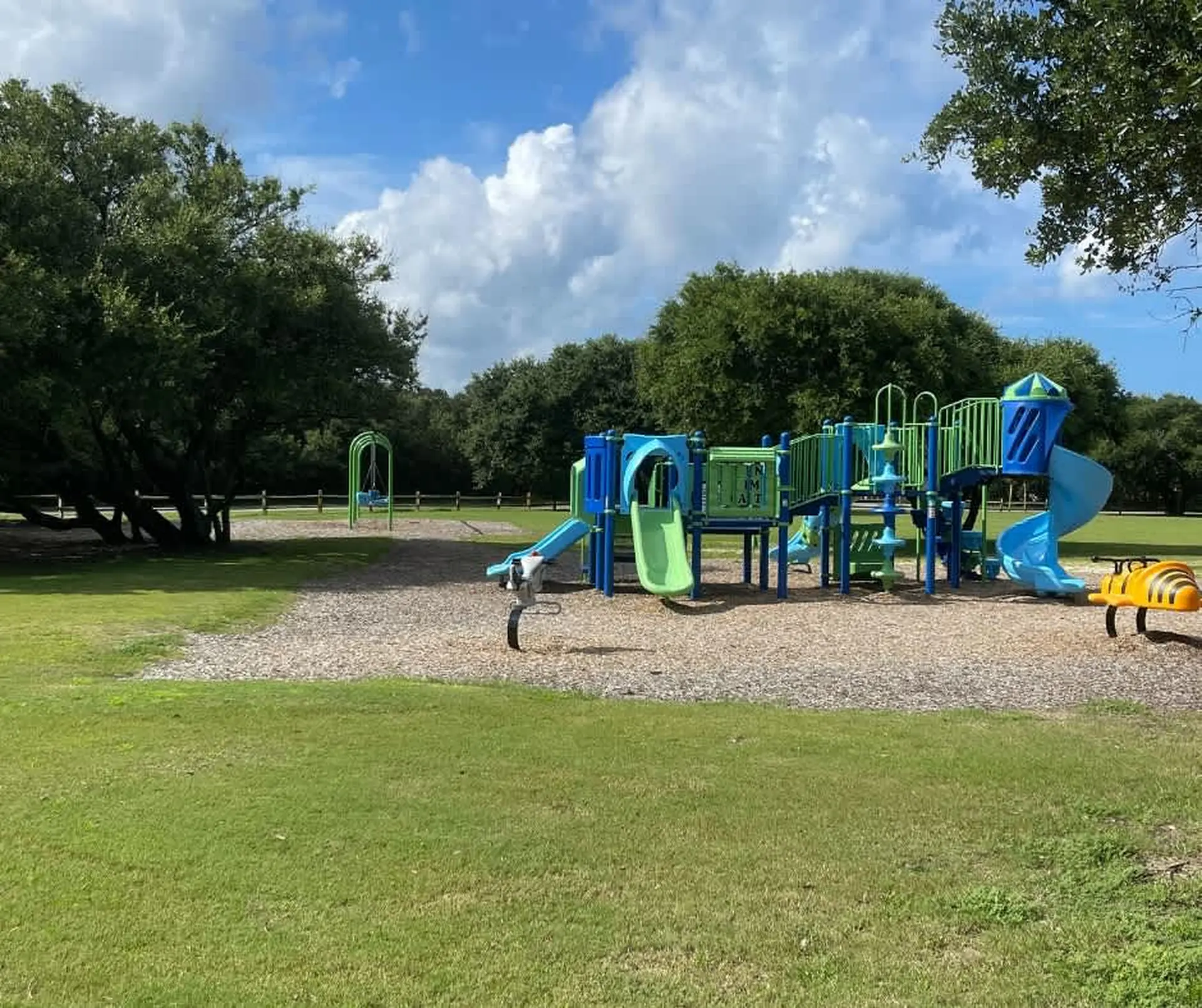 A colorful playground with blue and green slides, swings, and jungle gym.