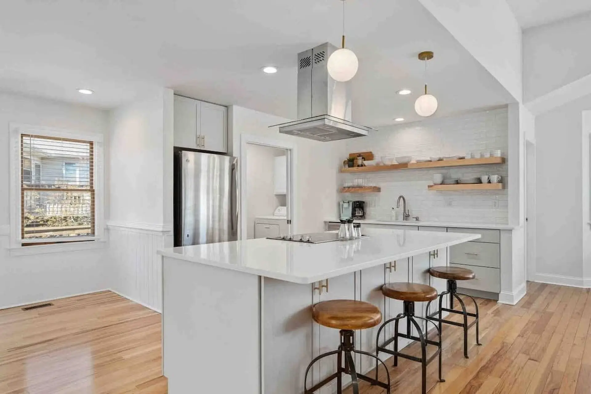 Modern kitchen with white island, stainless steel appliances, and light wood flooring.
