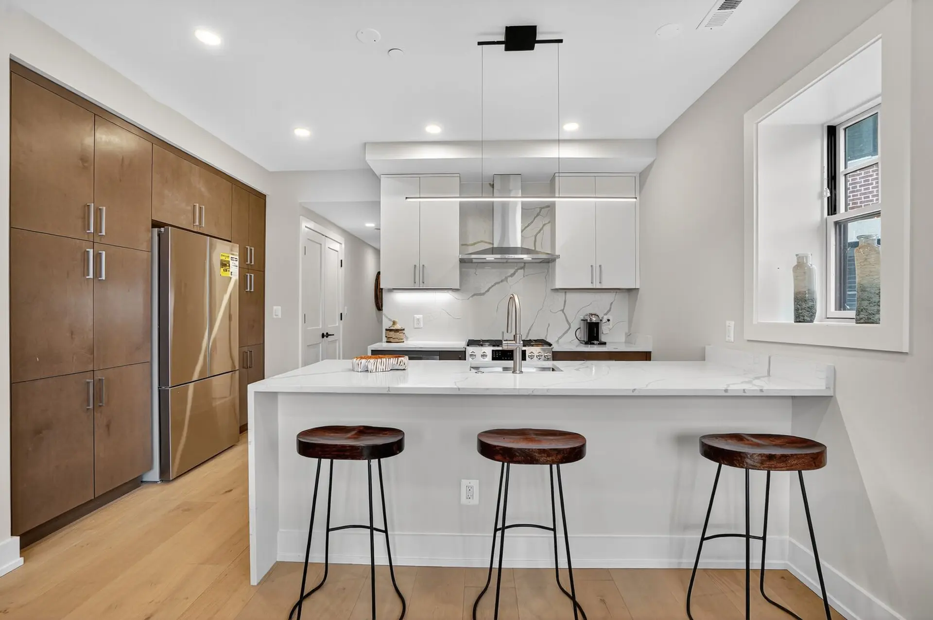 A modern kitchen with white marble countertops, stainless steel appliances, and wood cabinets.