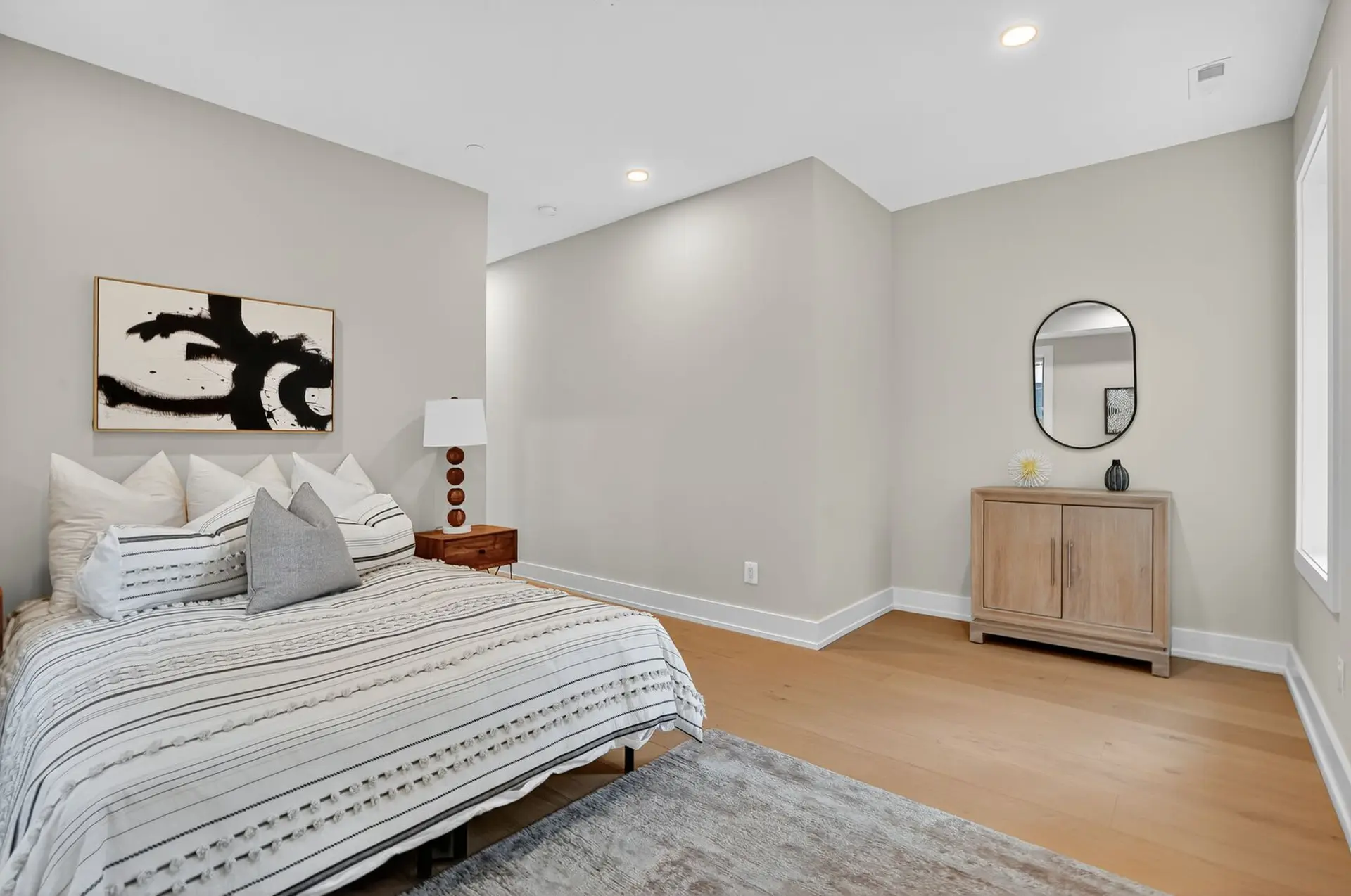 A minimalist bedroom with a bed, artwork, and a wooden dresser.