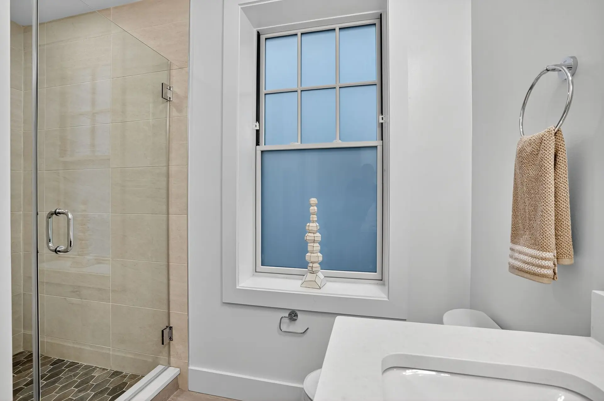 A modern bathroom with a shower, window, and sink.