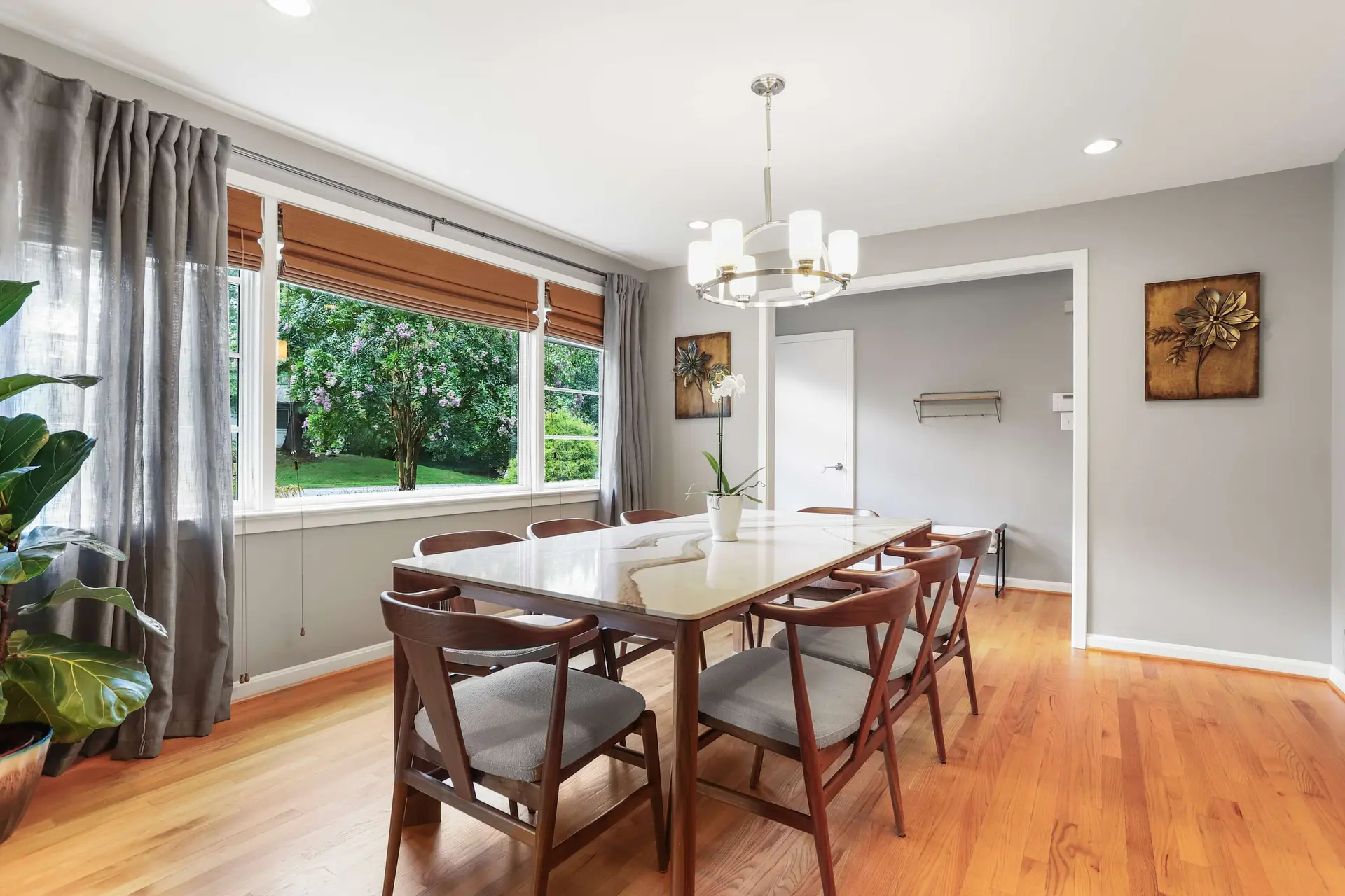 A dining room with a long table, chairs, and a large window overlooking a garden.