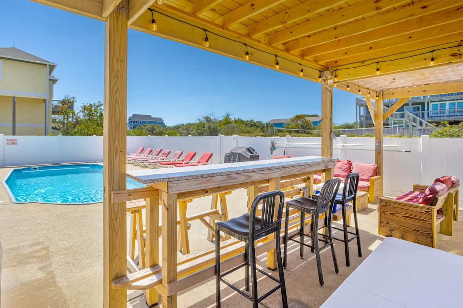 Outdoor bar with stools and lounge chairs by a pool.