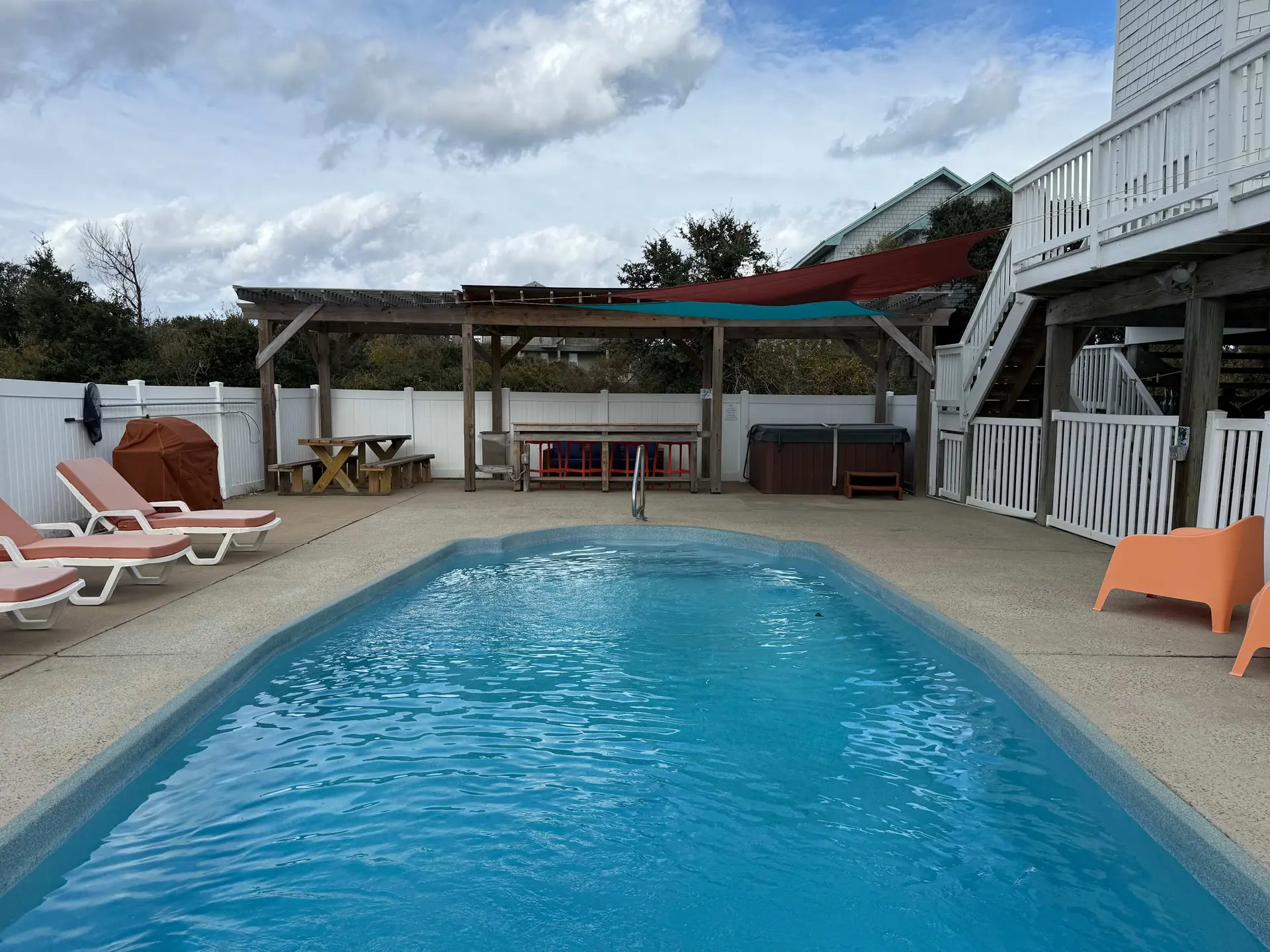 A pool with lounge chairs, hot tub, grill, and picnic tables under a pergola.