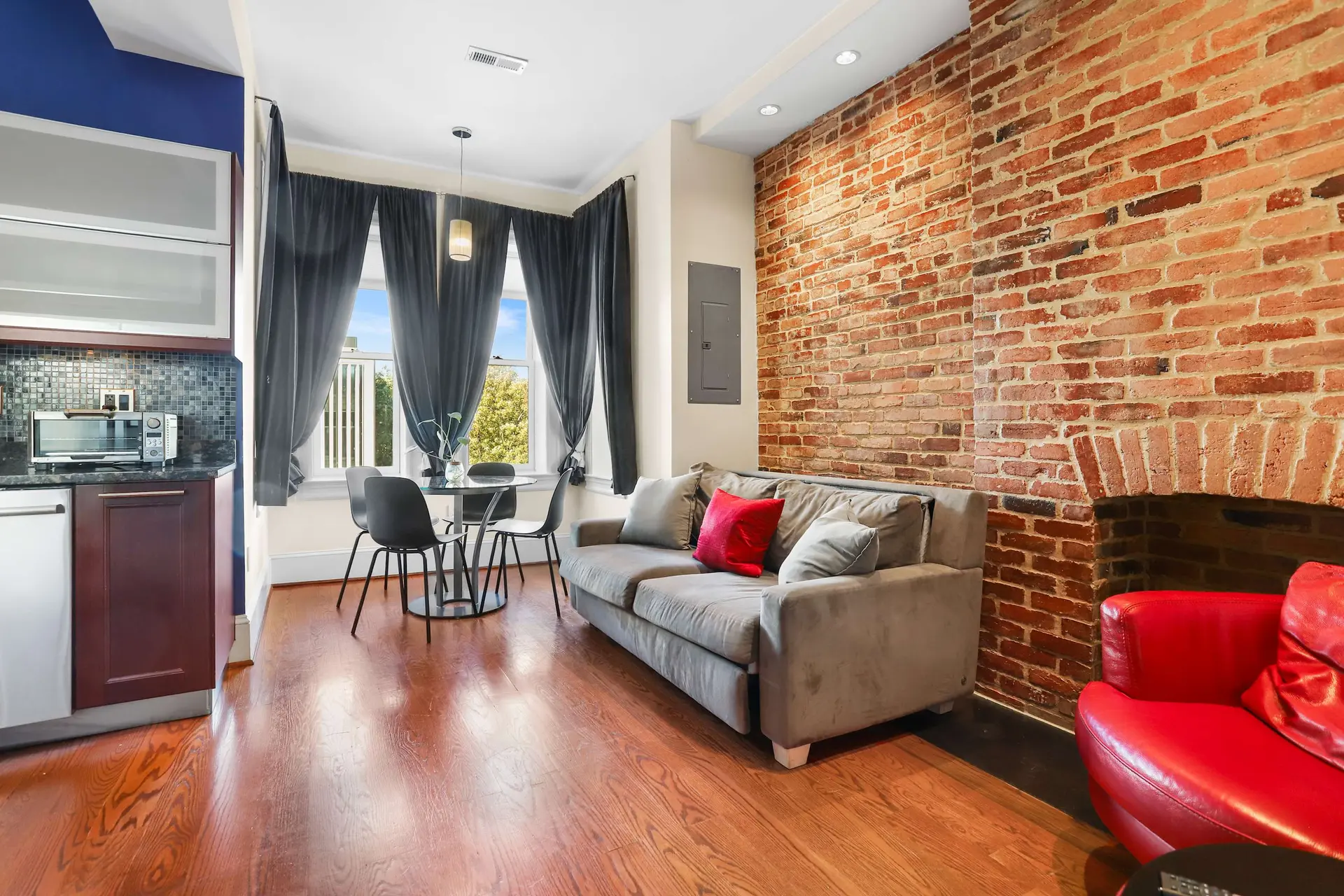 Living room with exposed brick wall, gray sofa, red armchair, and dining table.