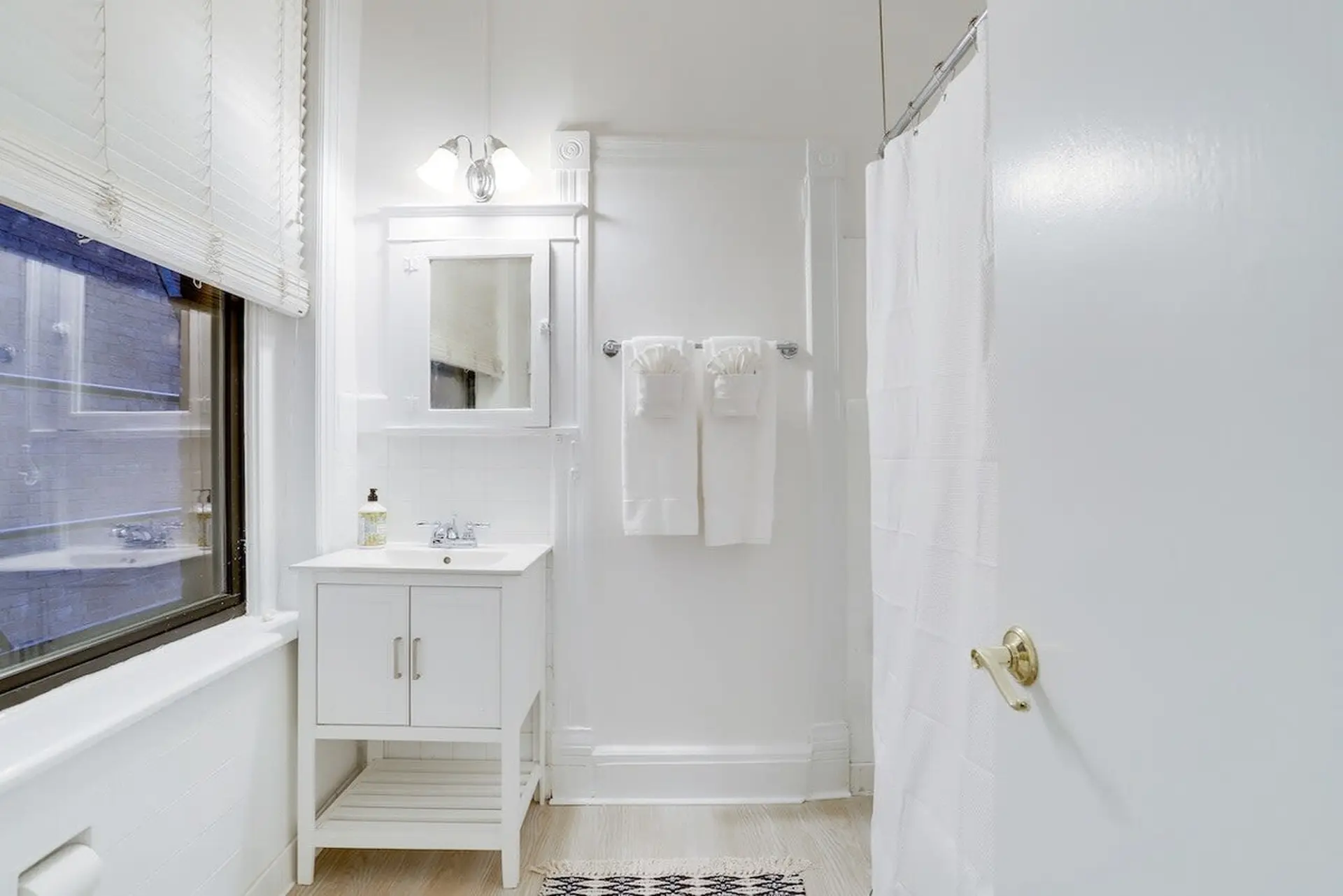 Bright, all-white bathroom with white vanity, mirror, and shower curtain.