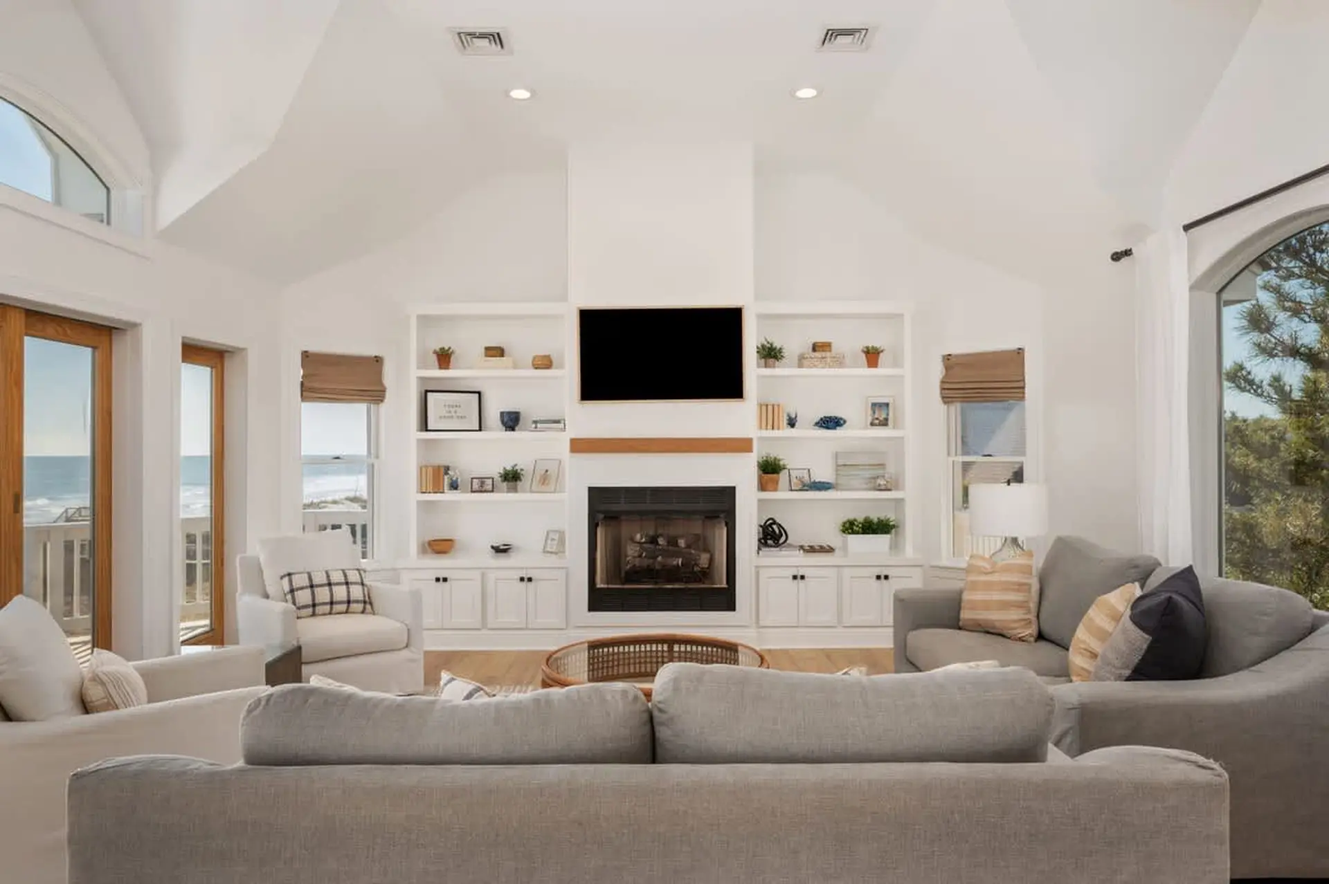 A bright living room with a fireplace and built-in shelves, overlooking the ocean.