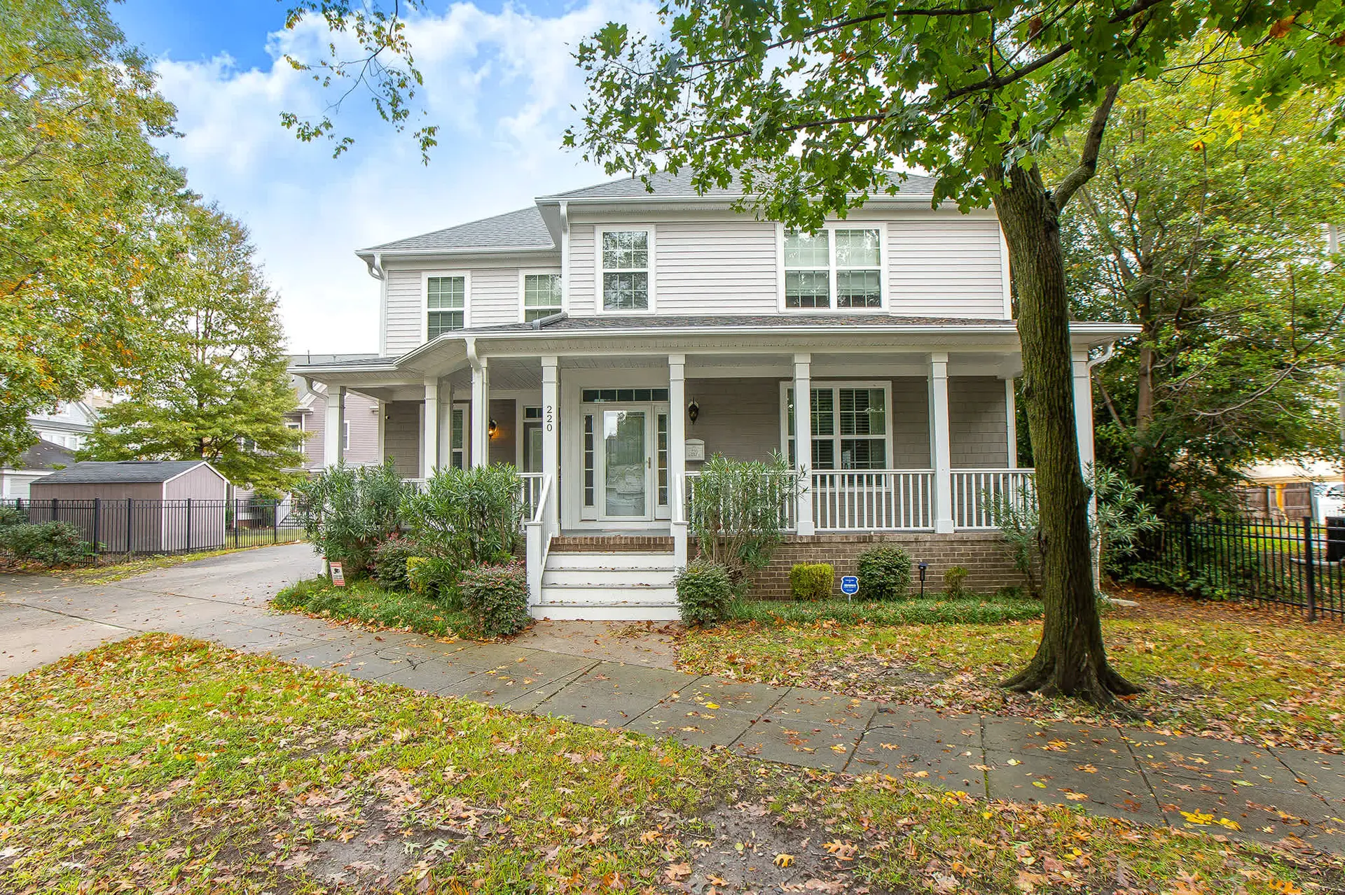 House with a wraparound porch, surrounded by trees and fallen leaves.
