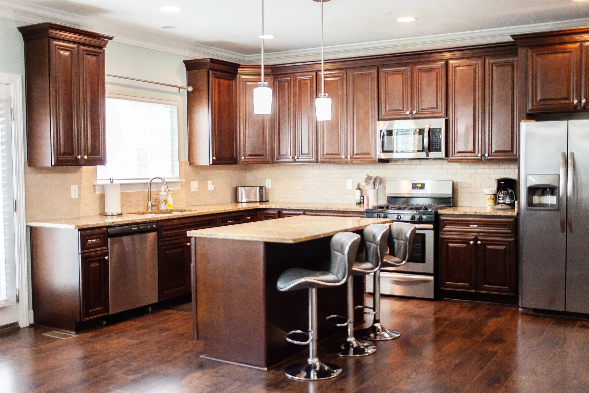 Kitchen with dark cherry cabinets, granite countertops, stainless steel appliances, and island bar.