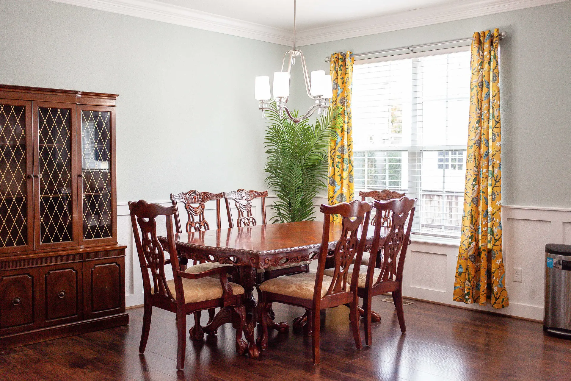 A dining room with a wooden table and chairs, a hutch, and yellow curtains.
