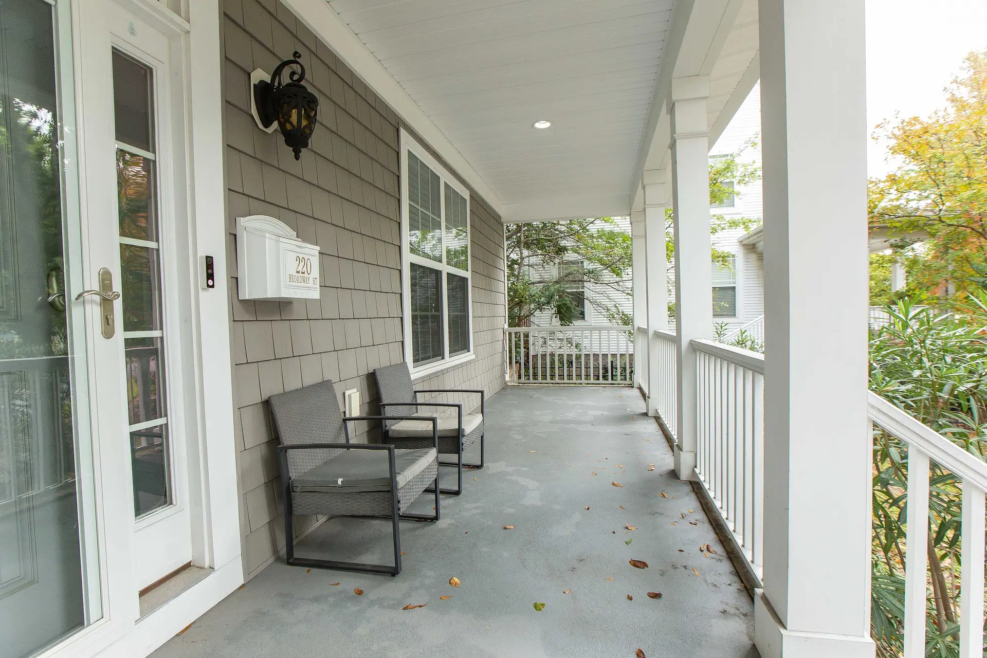 A covered porch with two chairs, a mailbox, and a white railing.