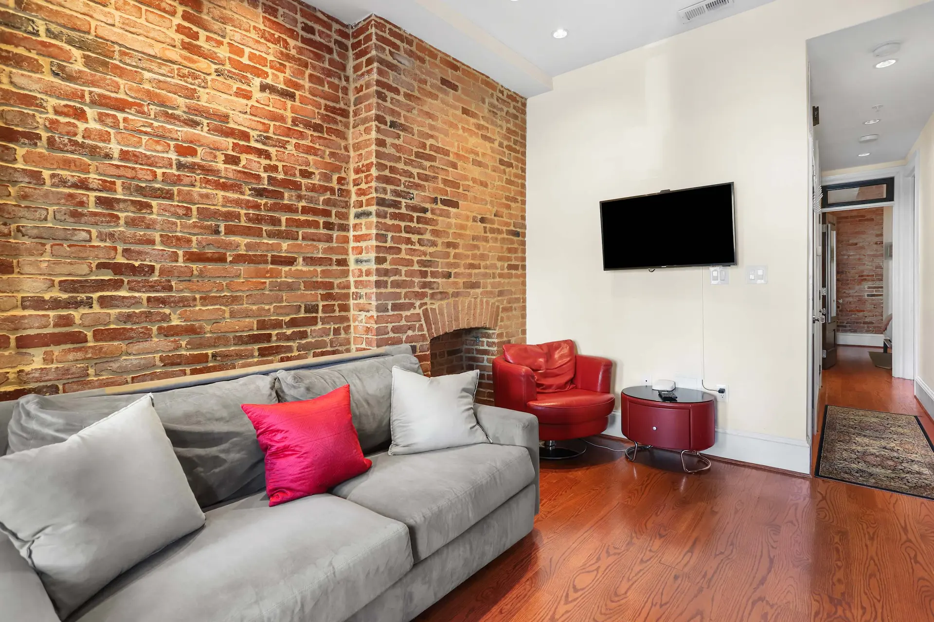 Living room with grey sofa, red armchair, and exposed brick wall.