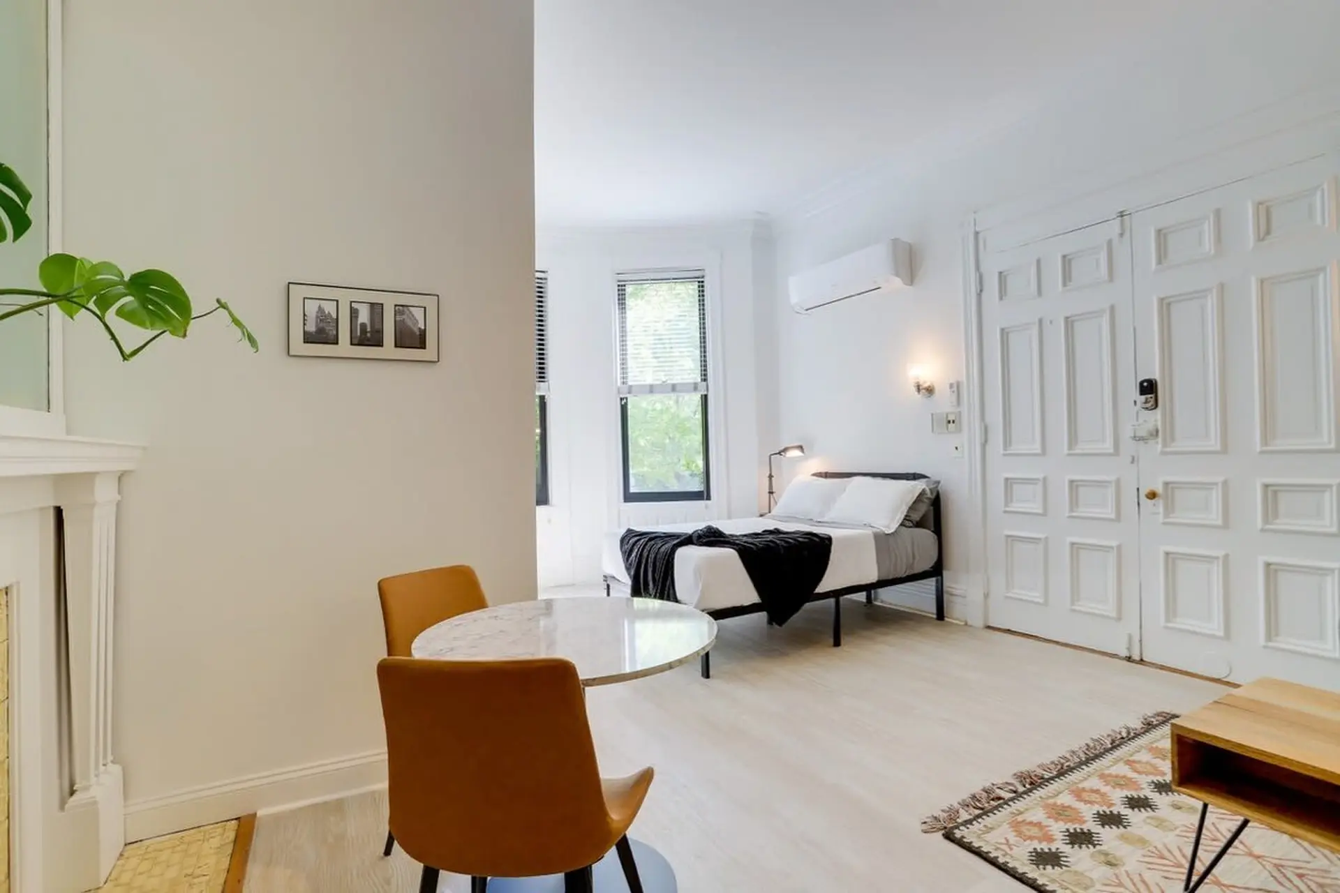 A bright studio apartment with a bed, dining table and chairs, and a fireplace.