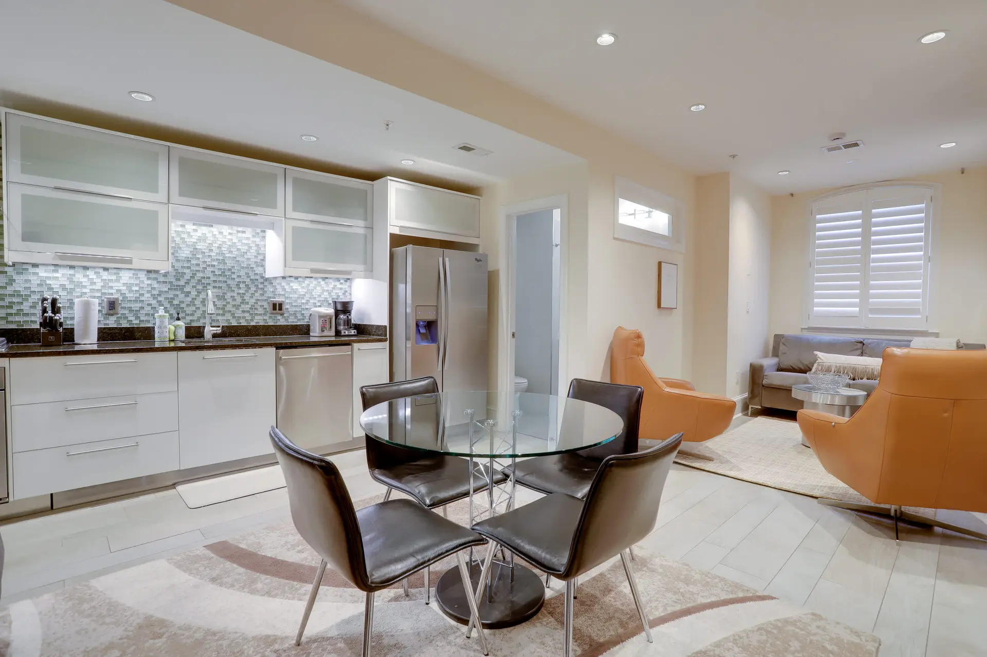 An open-concept living and kitchen area with modern furnishings and glass-top dining table.