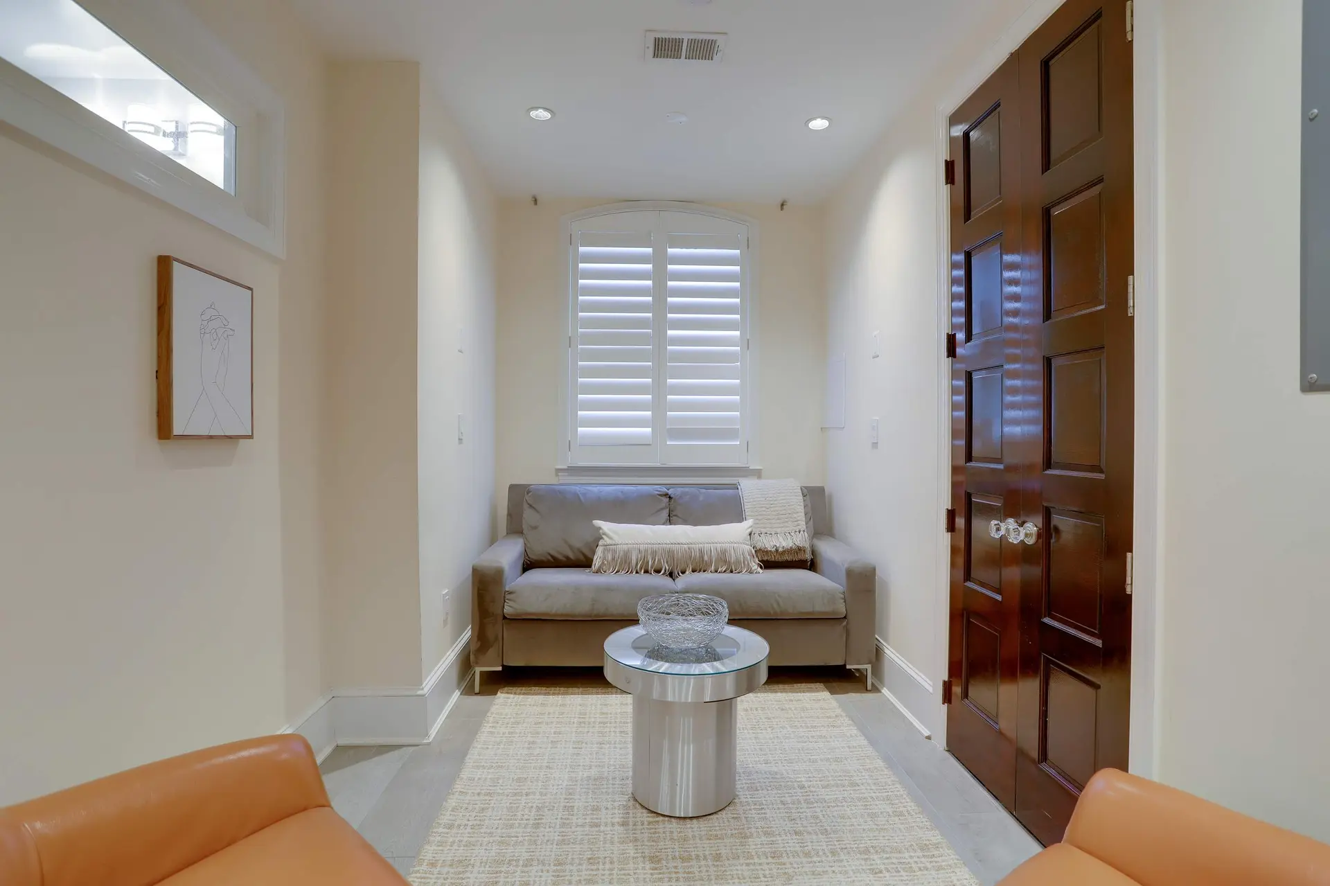 A small, beige room with a couch, a coffee table, a rug, and a wooden door.
