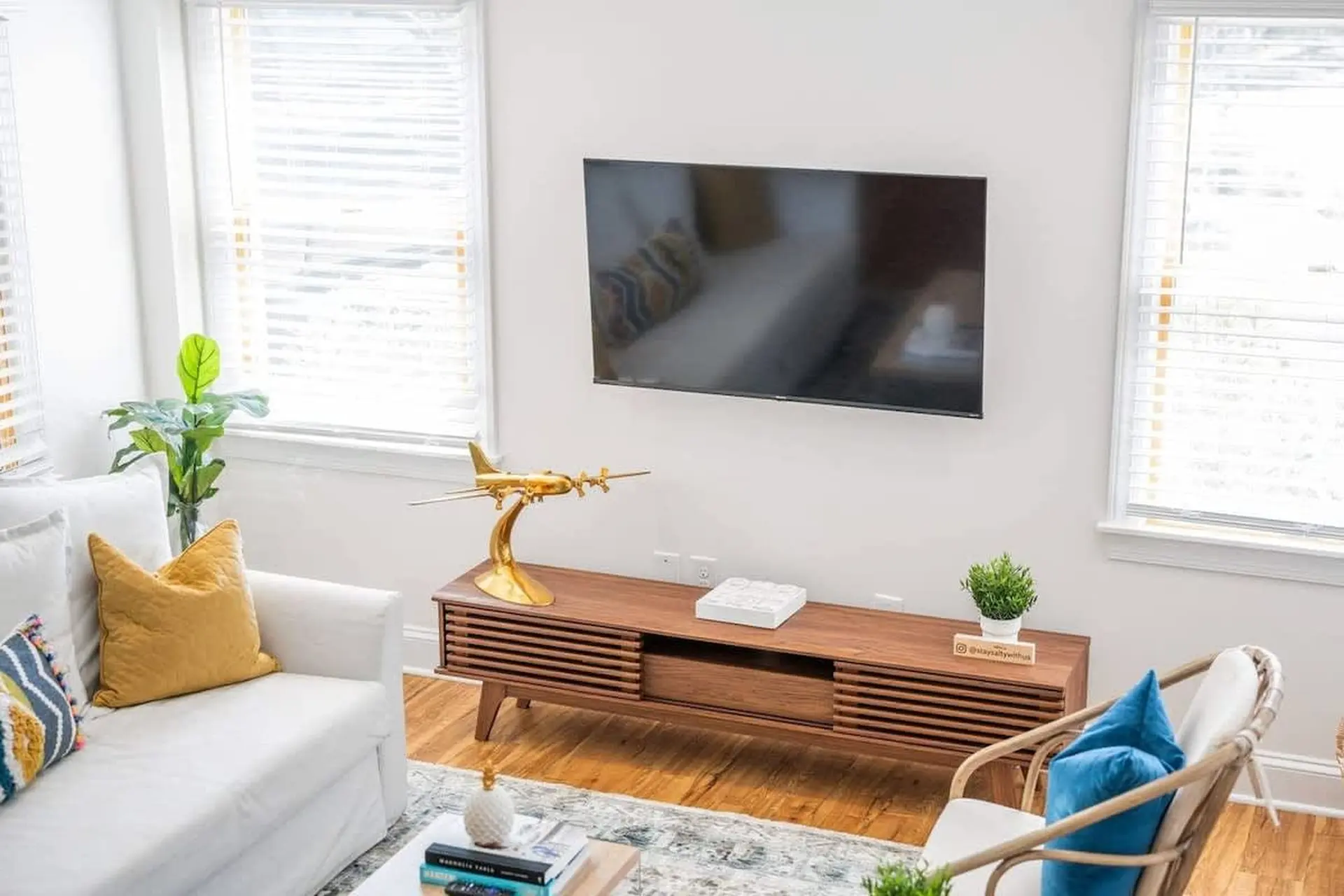 A living room with a white couch, a modern TV stand, and a TV mounted on the wall.