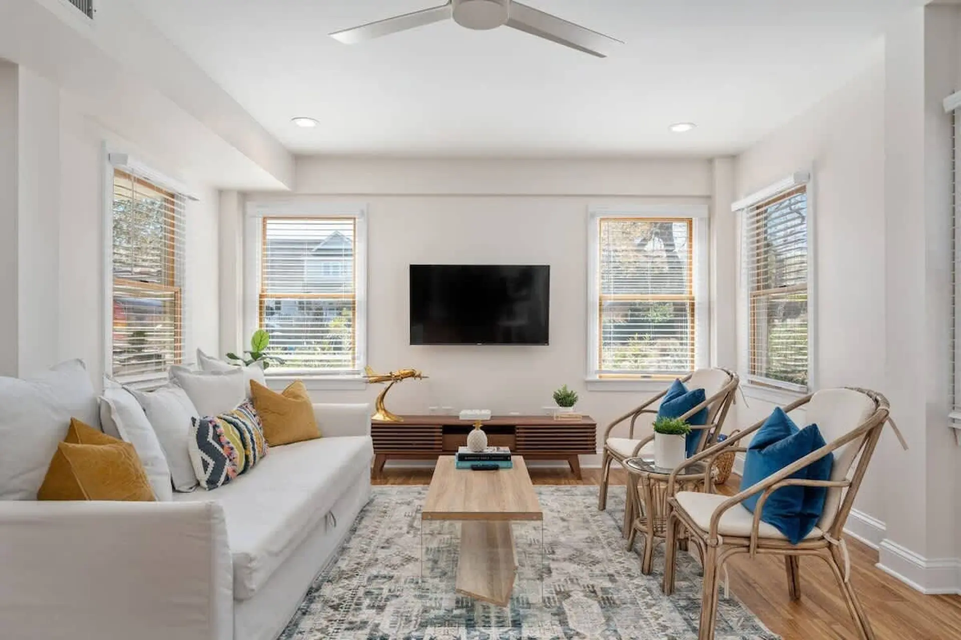 A living room with a white sofa, a modern media console, and two rattan chairs.