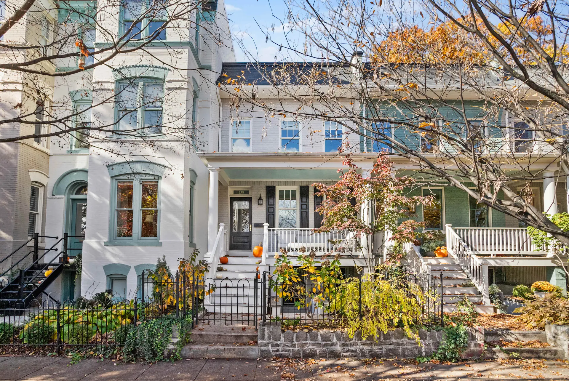 Fall scene of a row house with colorful foliage and pumpkins.