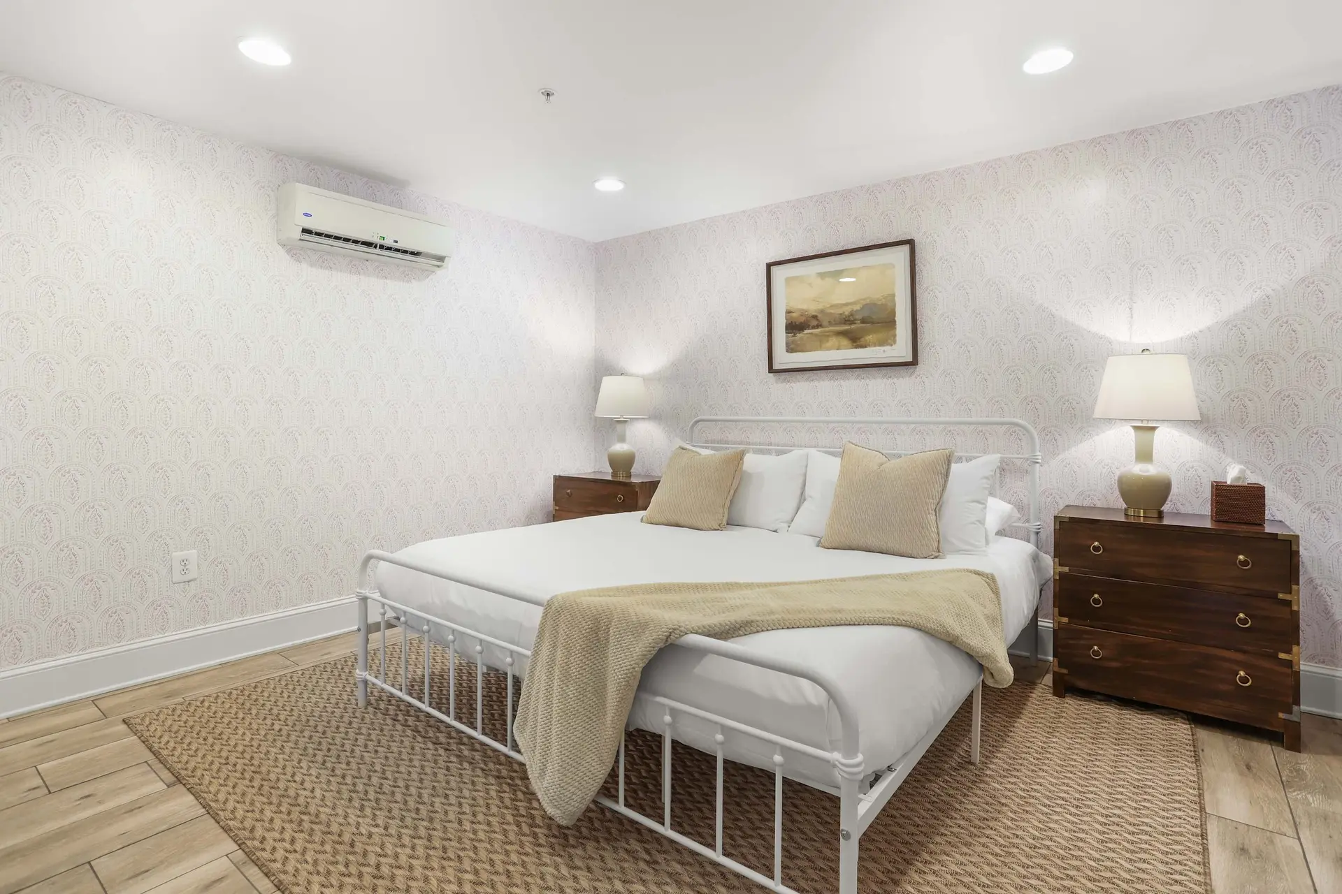 A bedroom with a white metal bed, patterned wallpaper, and wooden floors.