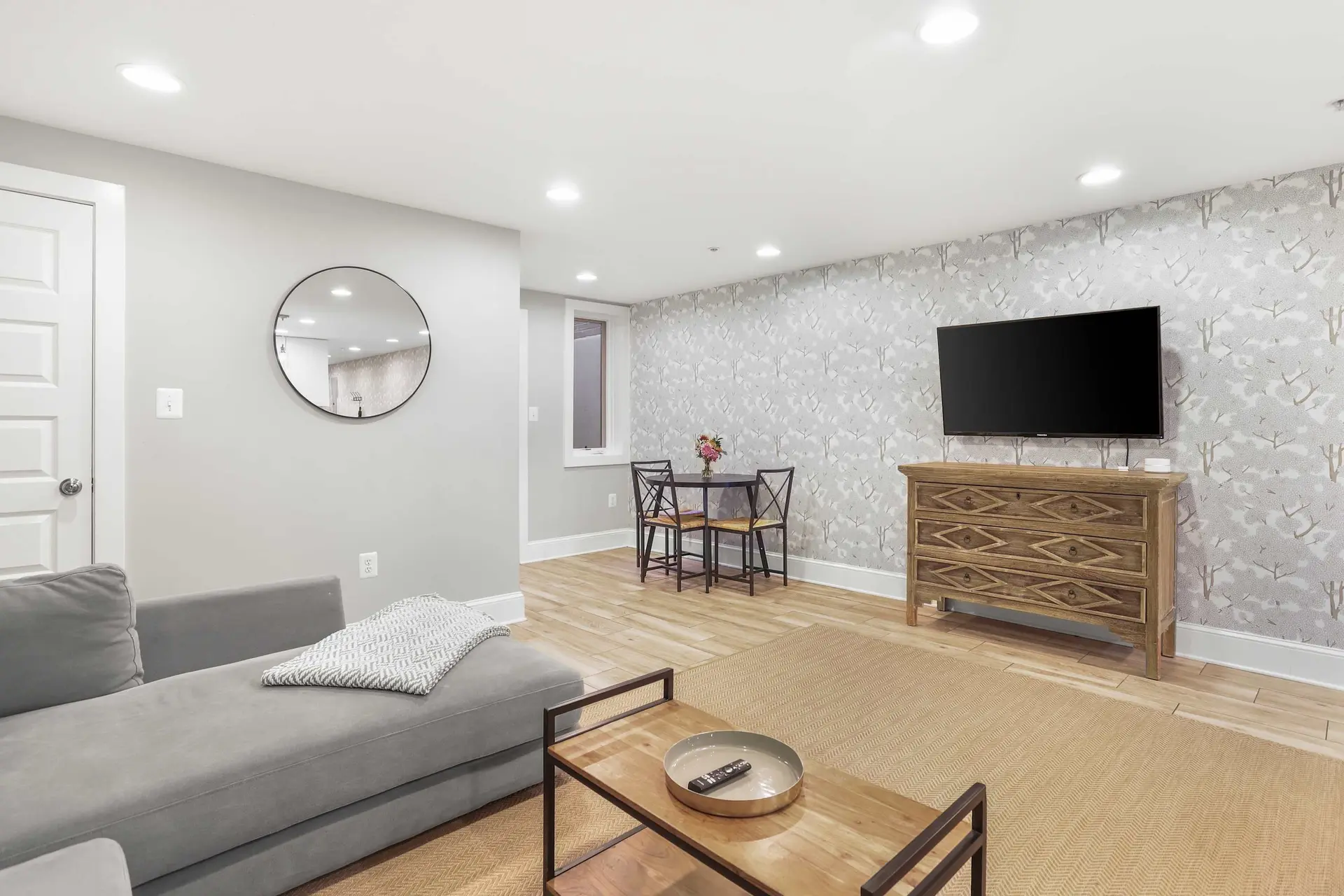 Modern living room with gray sofa, wooden dresser, and TV on a floral wallpapered wall.