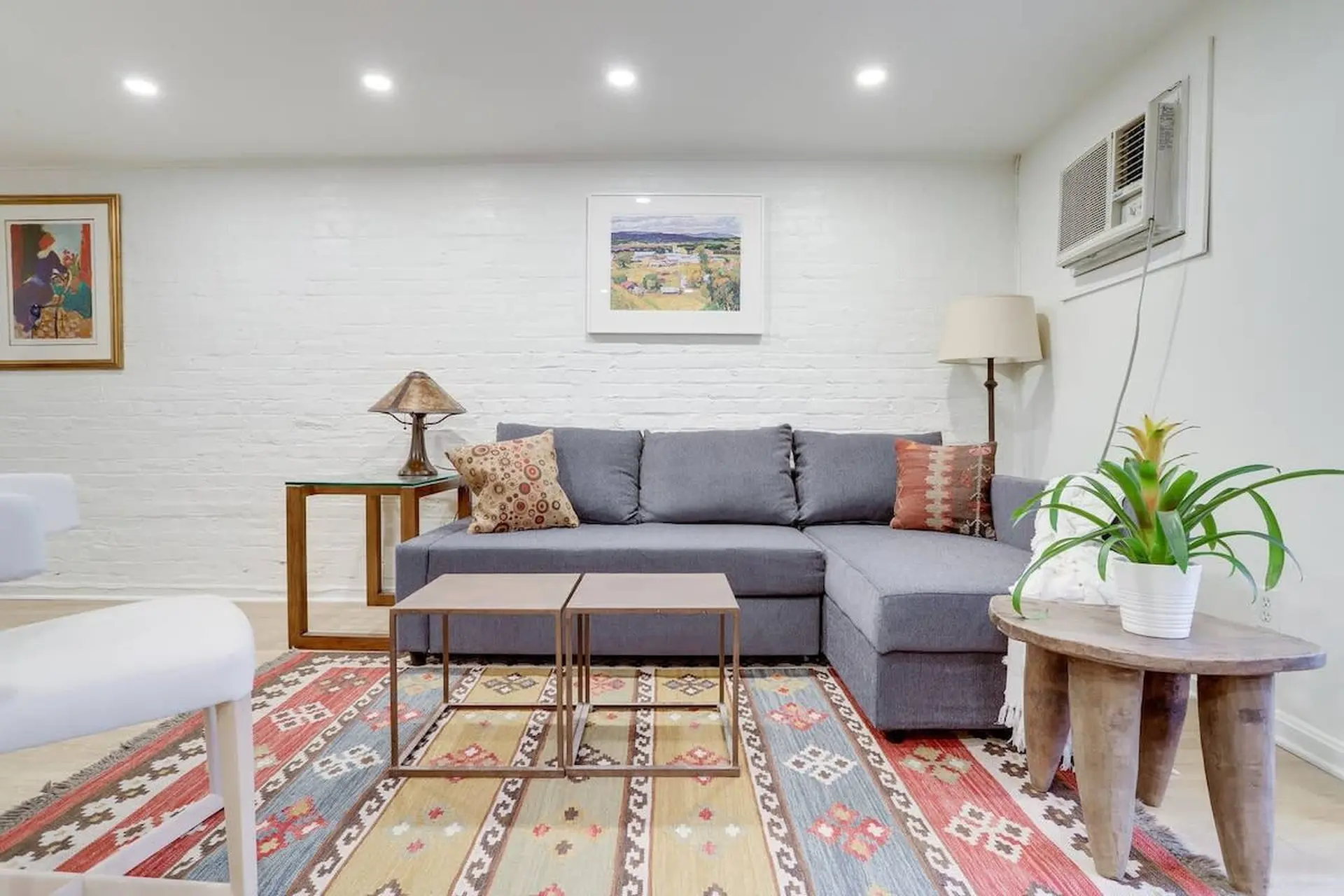 Living room with gray sectional couch, colorful rug, and a plant on a wooden table.
