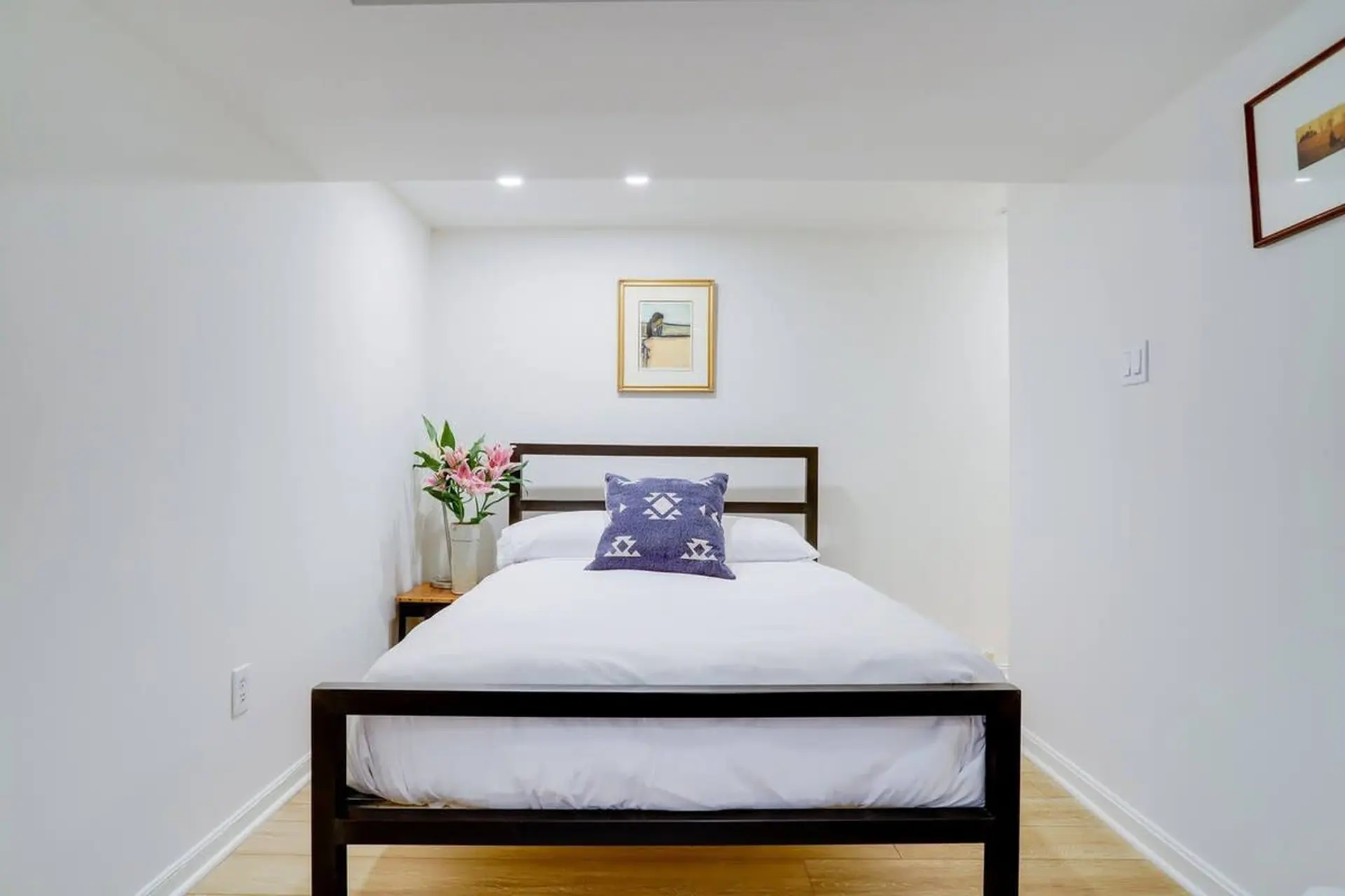 A modern bedroom with a dark brown bed frame, white linens, and a patterned pillow.