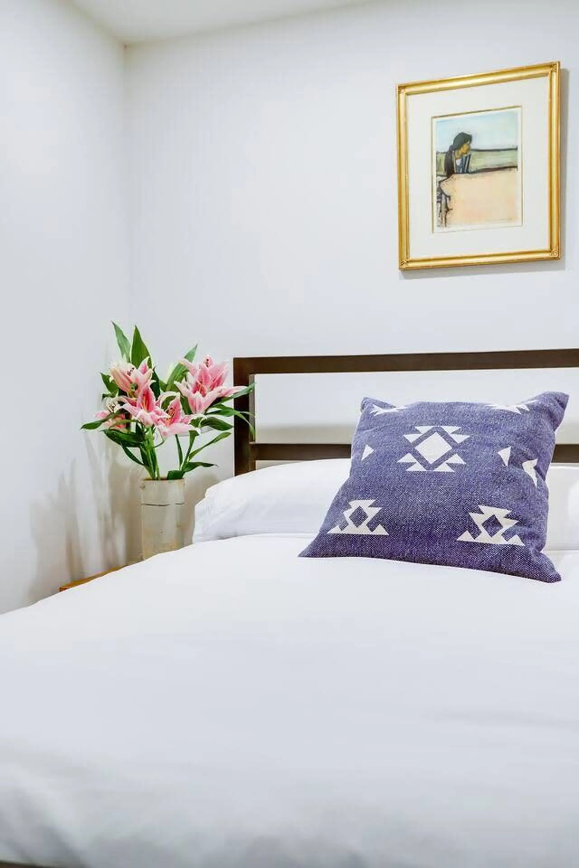 A bed with white sheets and a purple pillow with a geometric pattern.