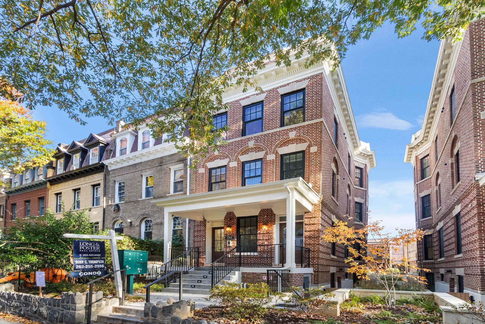 A stately brick condo building with a large porch and windows sits under a tree.