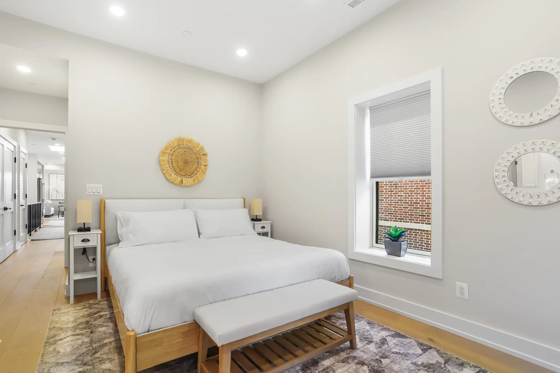Bedroom with a white bed, a wooden bench, and two circular mirrors.