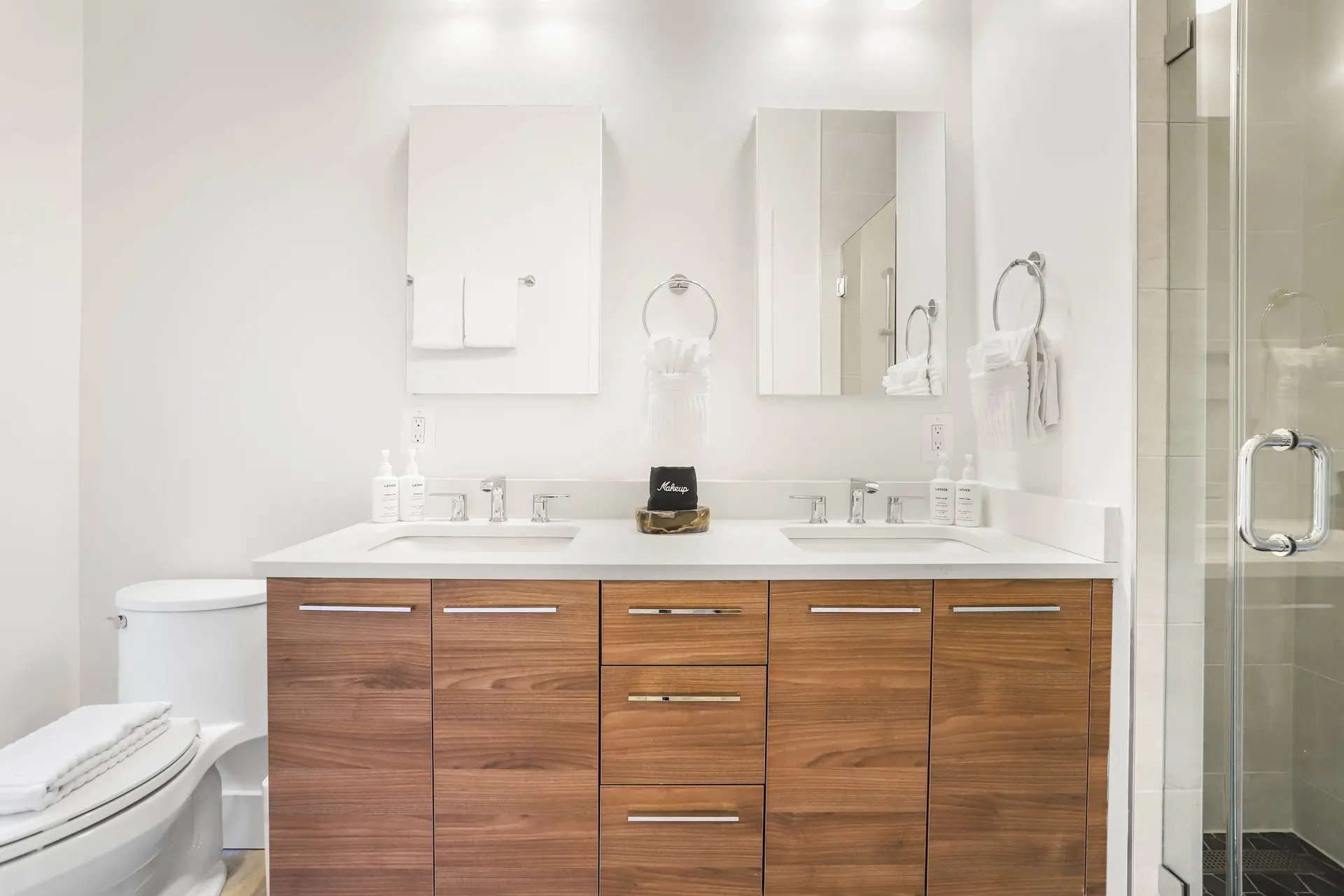A modern bathroom with a double vanity, toilet, and glass shower.