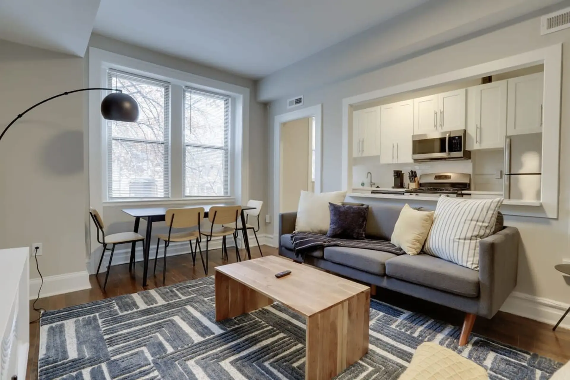 A modern living room with a grey sofa, coffee table, dining set, and an open kitchen.