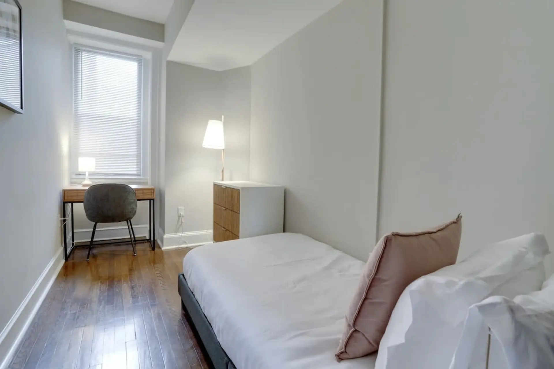 A bed with white bedding and pink pillows sits next to a nightstand.