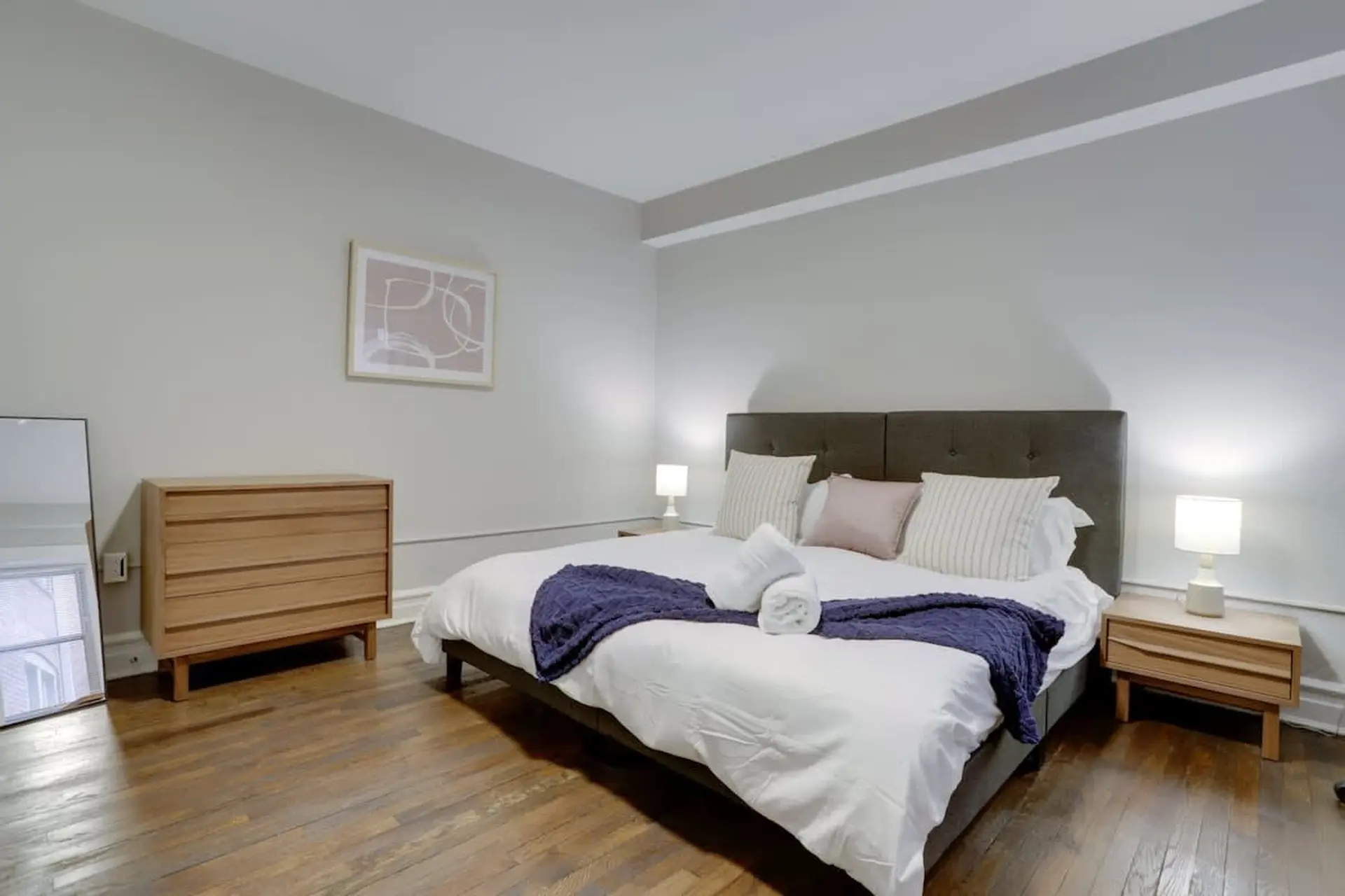 A modern bedroom with a king-sized bed, wooden dresser, and minimalist decor.