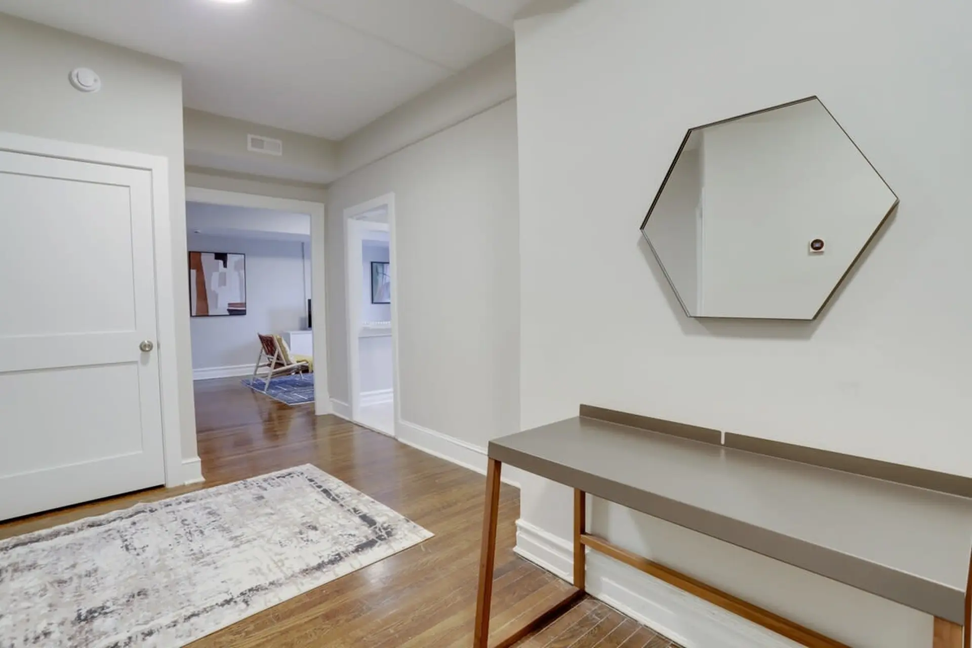 A modern hallway with a gray console table, a hexagonal mirror, and a white door.
