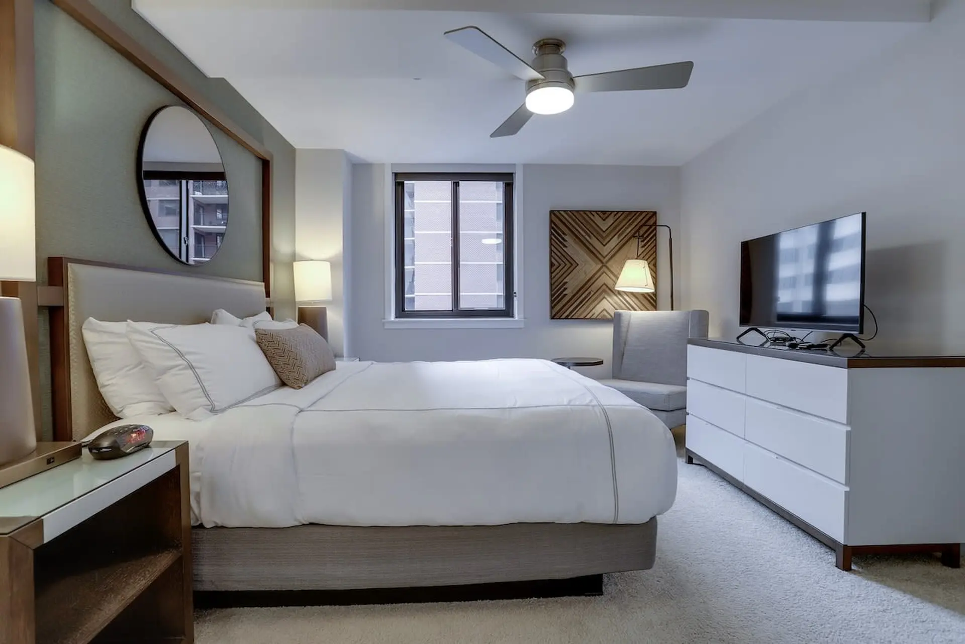 A modern bedroom with a large bed, TV, and a ceiling fan.