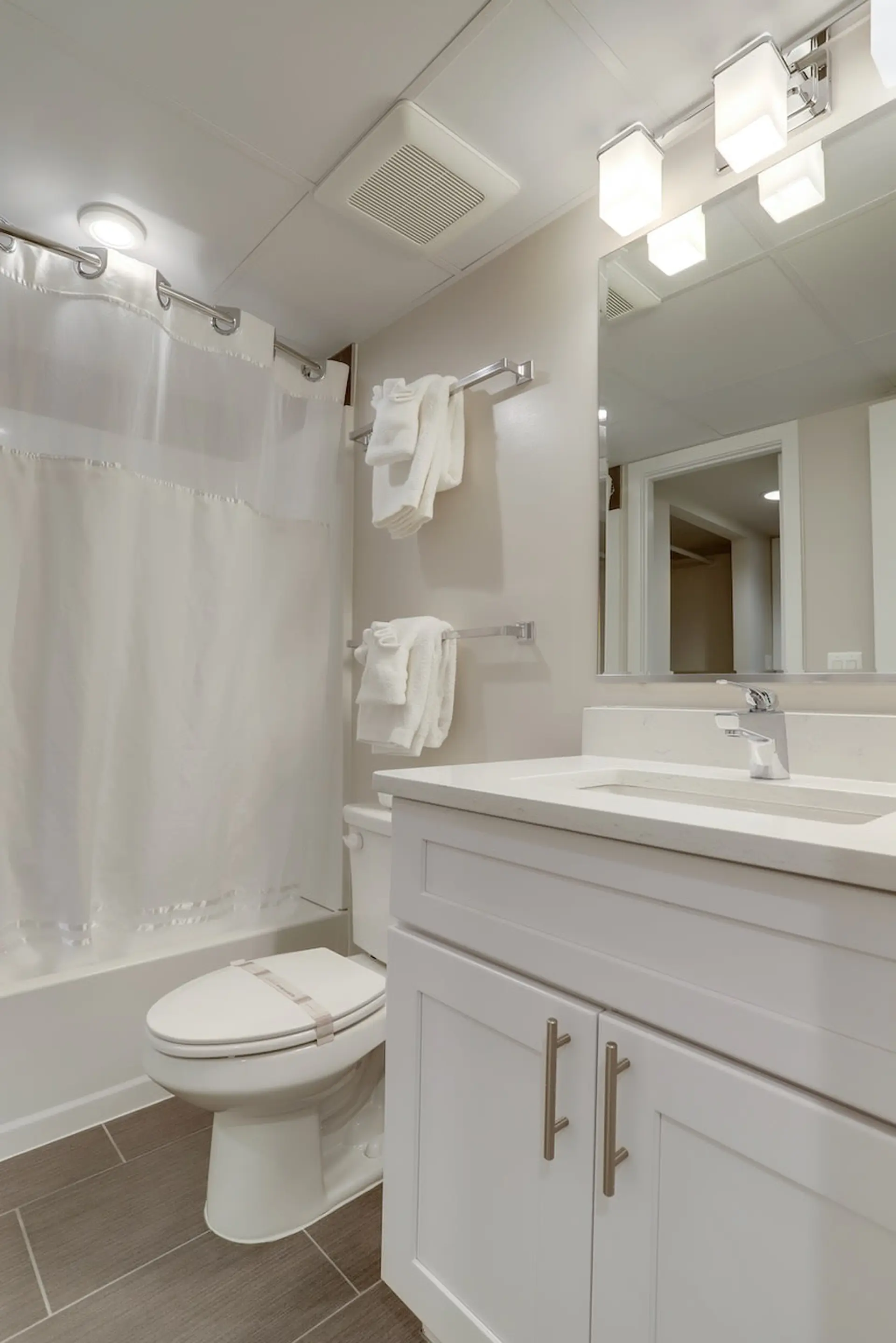 A clean, modern bathroom with a white toilet and vanity, and a white shower curtain.