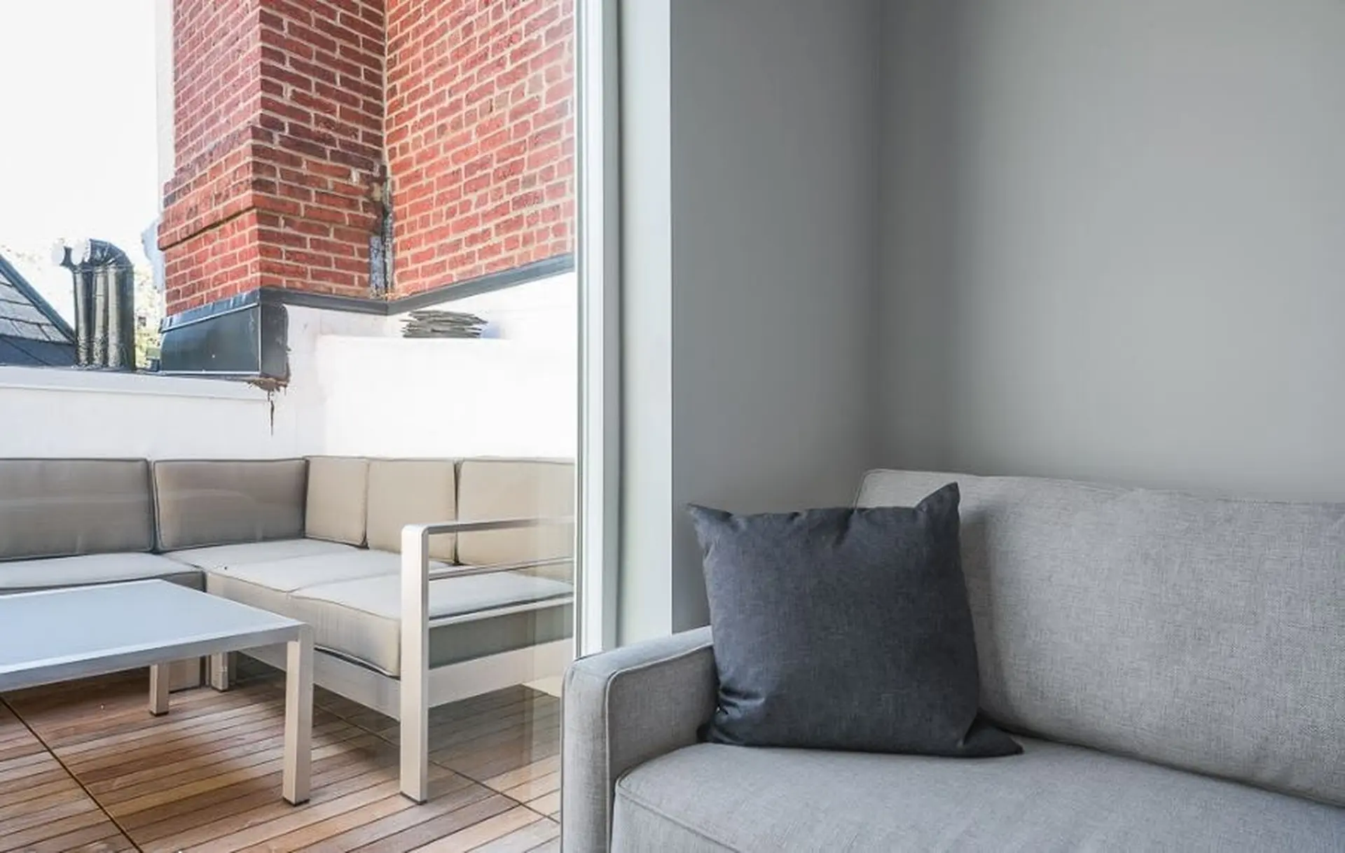 A sectional outdoor sofa with a coffee table on a wooden deck, next to a brick wall.