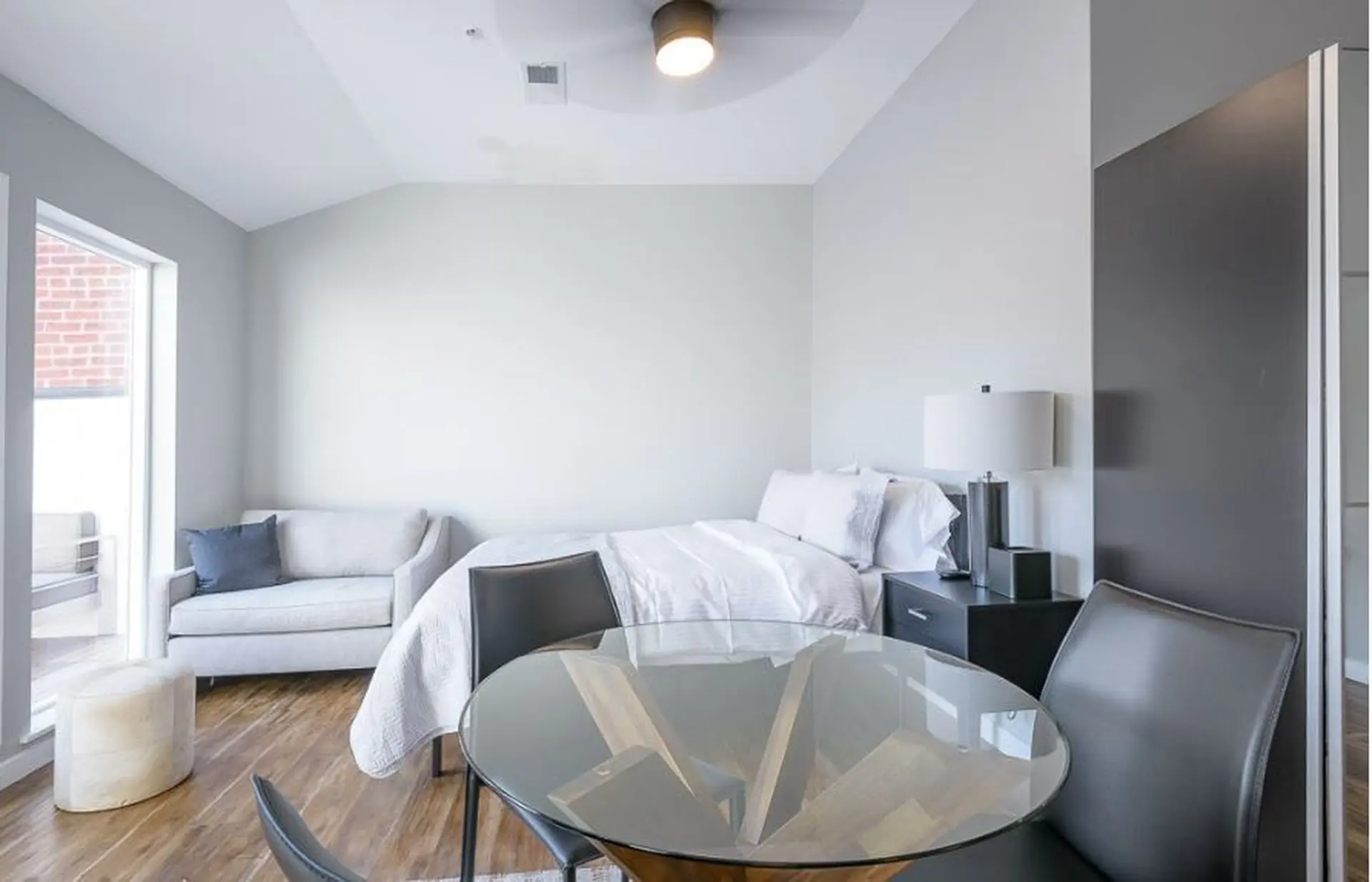 A studio apartment with a bed, sofa, dining table, and large window.