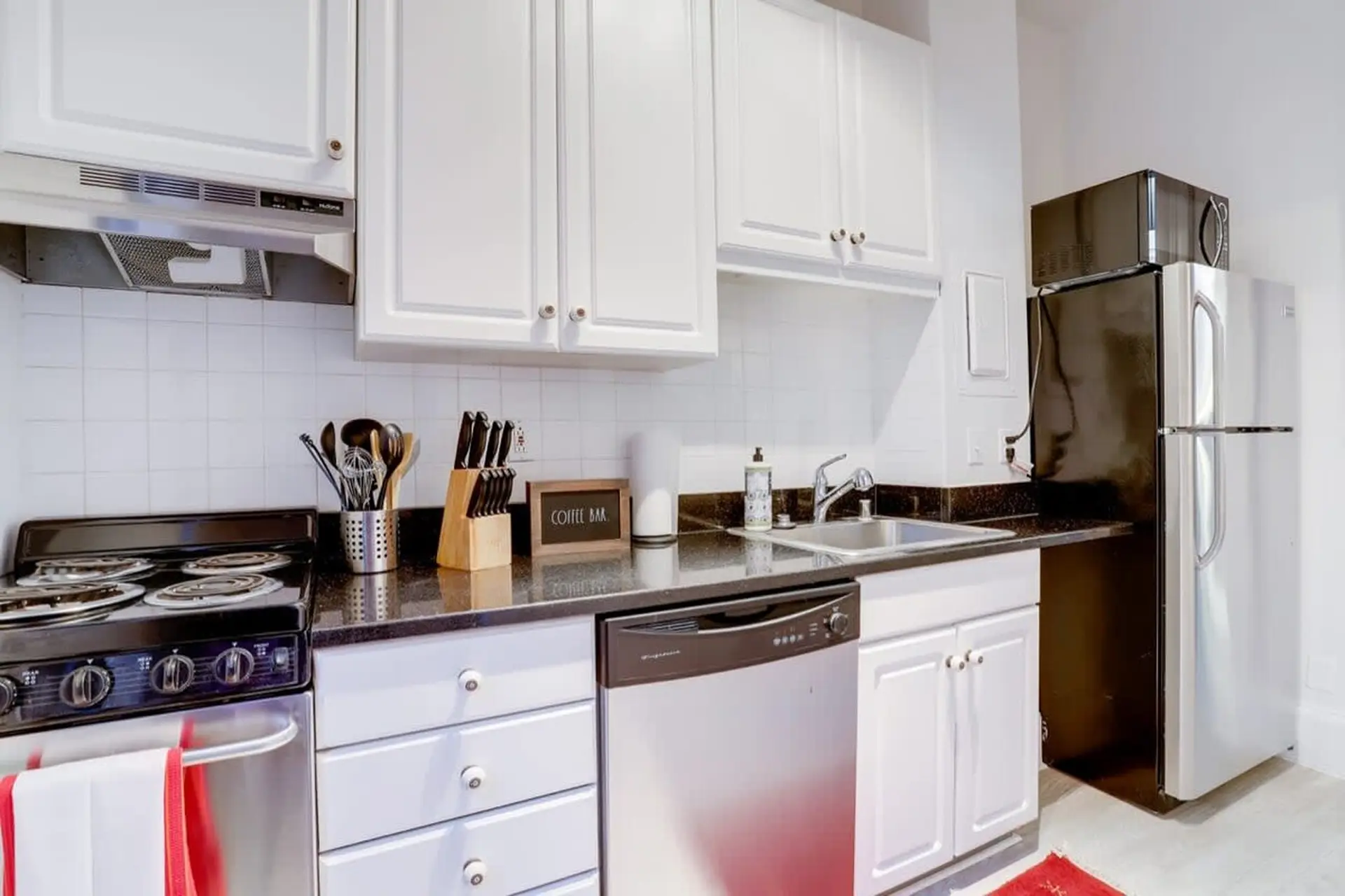 A modern kitchen with white cabinets, black countertops, and stainless steel appliances.