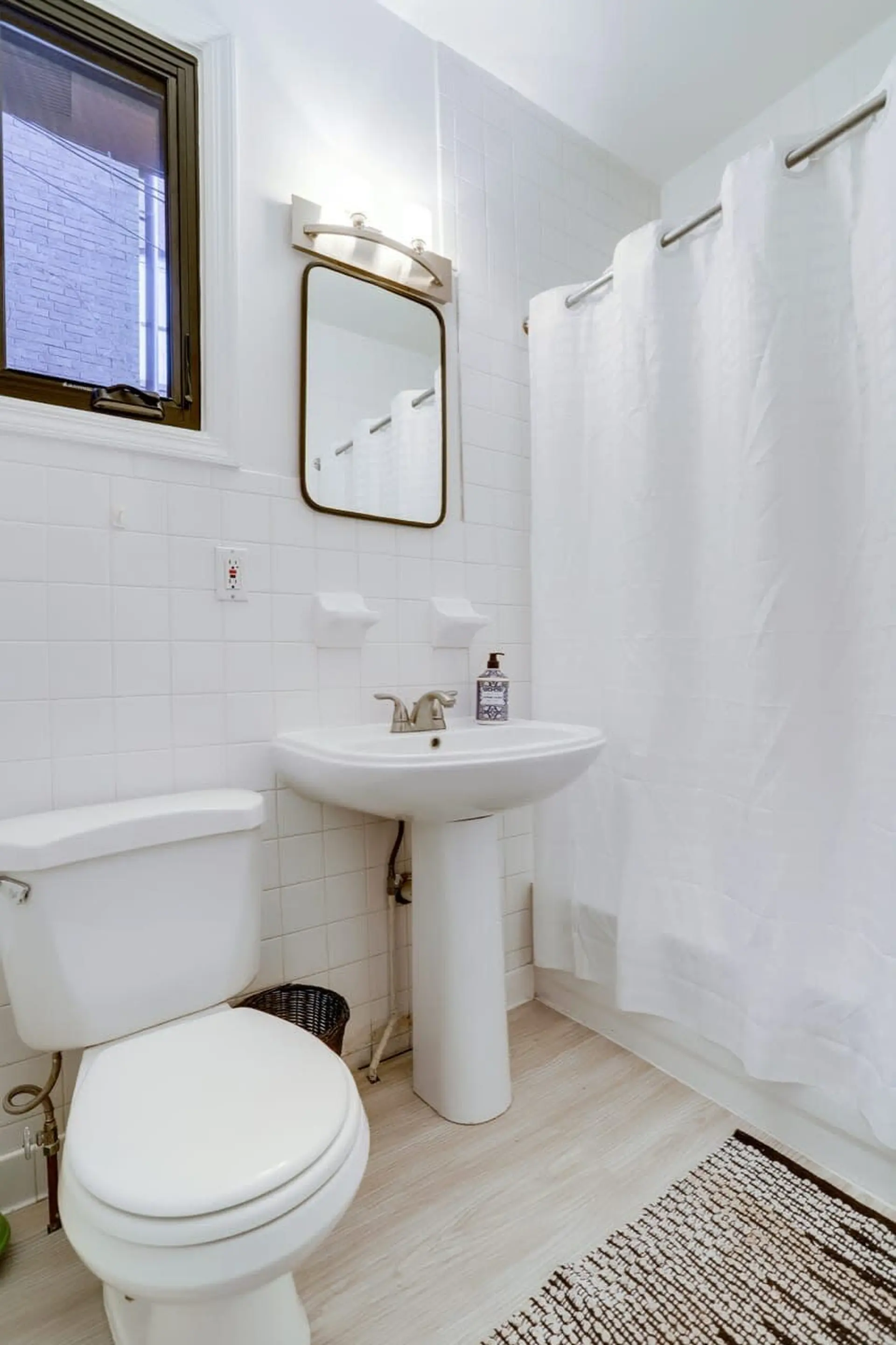 A bathroom with a toilet, pedestal sink, white shower curtain, and a window.