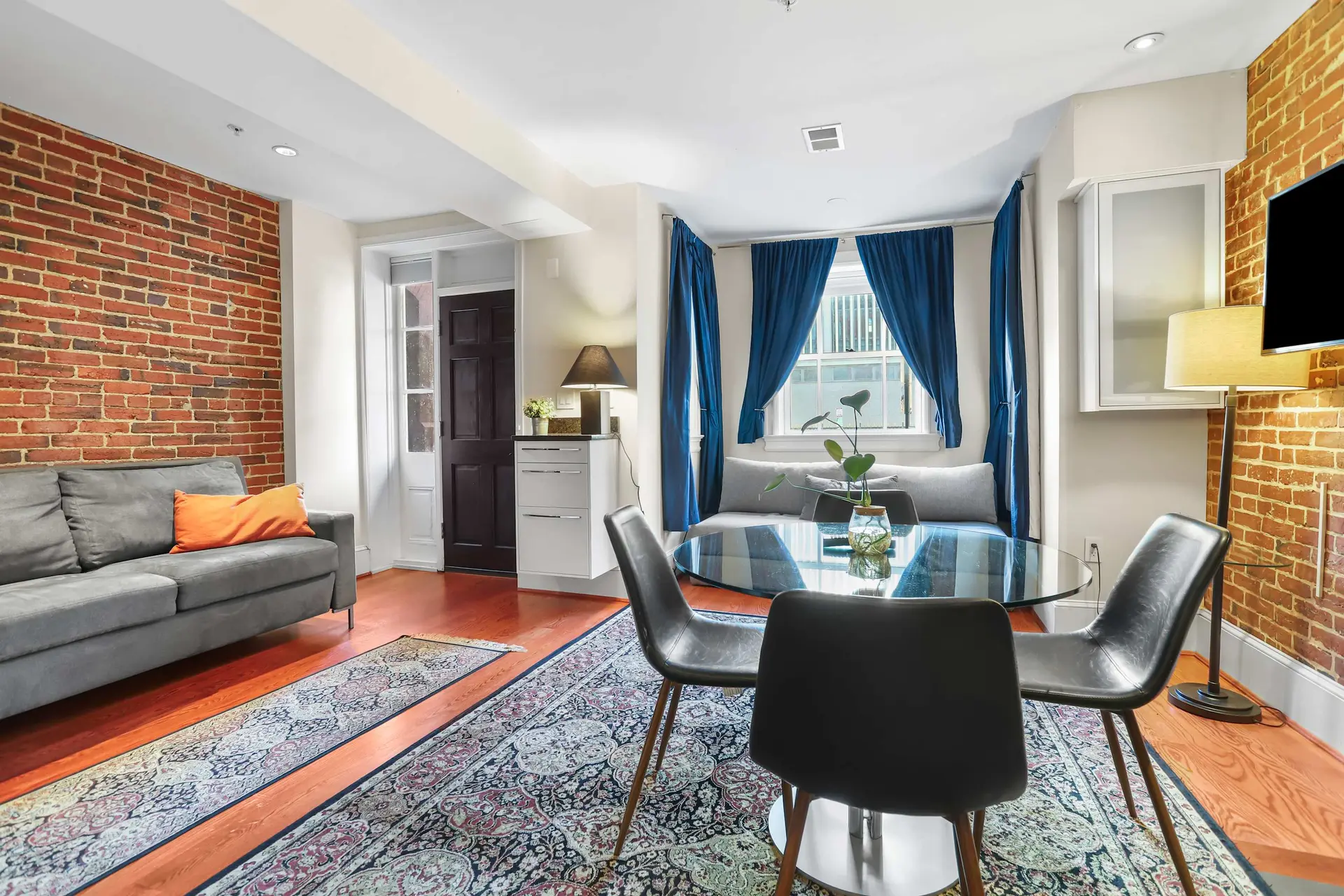 A living room with brick walls, a sofa, and a dining area with a round table.