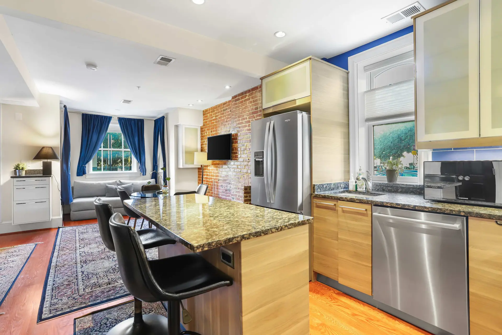 Modern kitchen island with granite countertop and bar stools, adjacent to a living area with blue cu