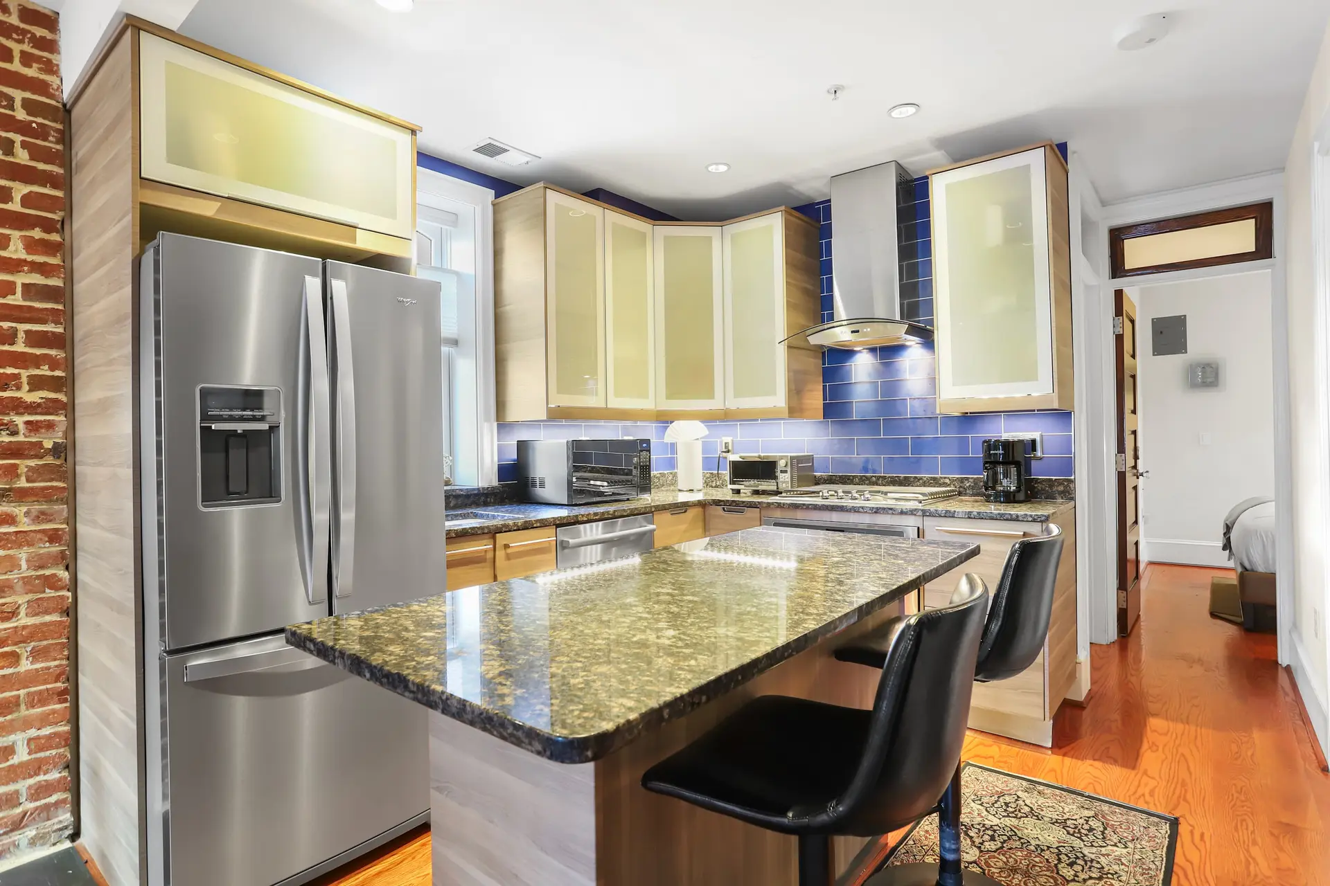 A modern kitchen with stainless steel appliances, granite countertops, and blue tile backsplash.