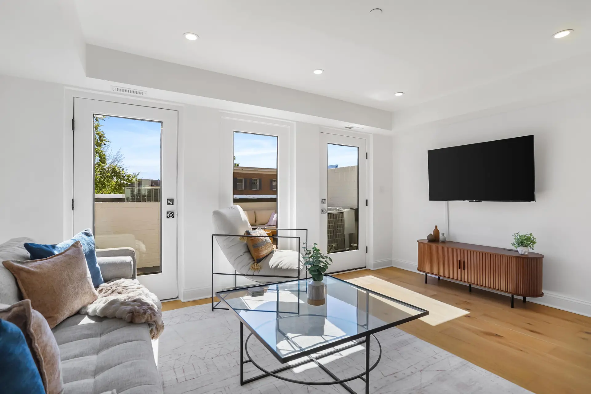 Modern living room with a sofa, glass coffee table, and a TV mounted above a wooden media console.