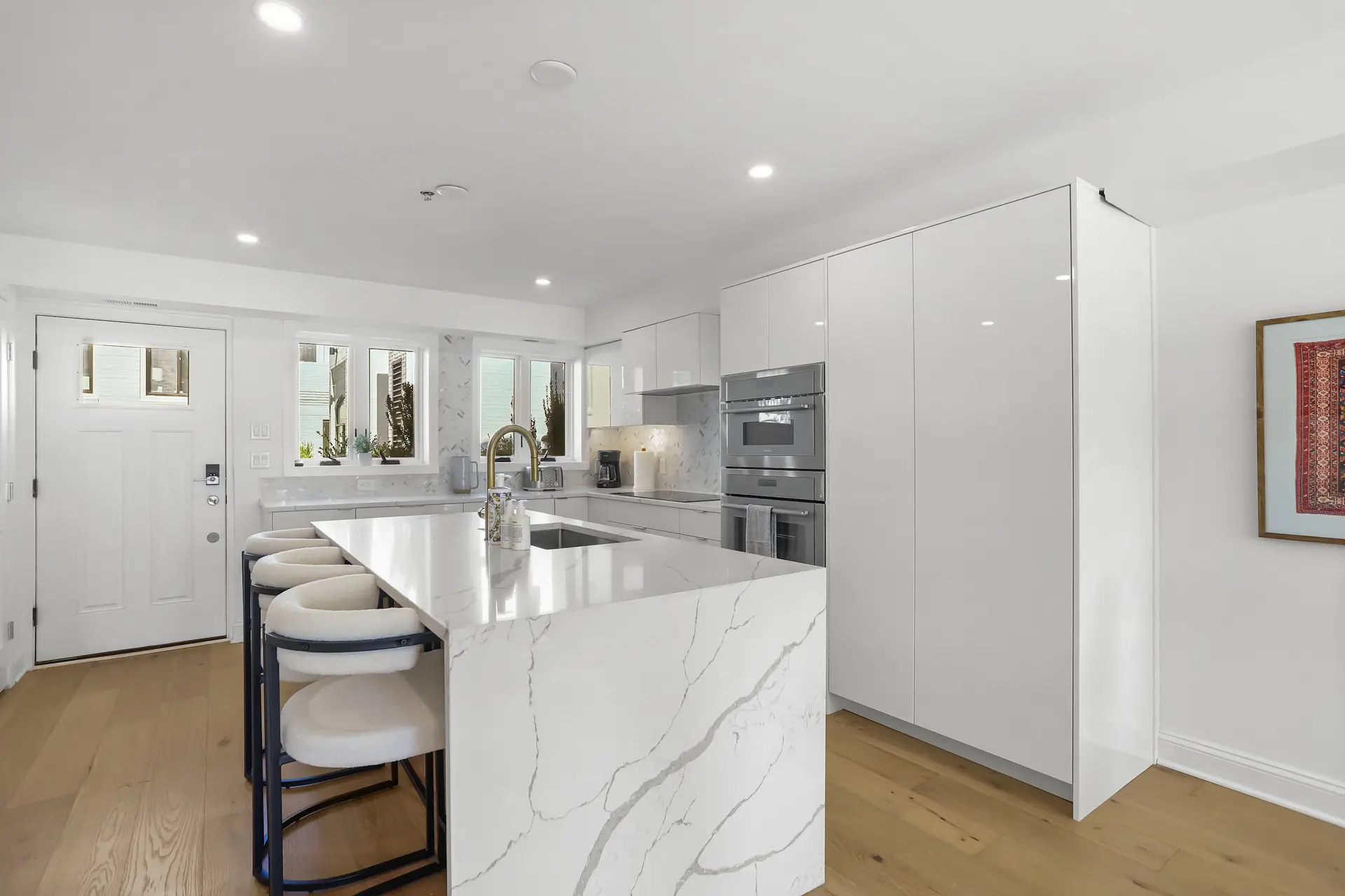 Modern white kitchen with marble island and stainless steel appliances.